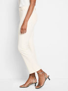 Off-white cropped demi-boot pants on a model, side view. Smooth fabric, subtle leg flare at ankle, belt loops visible.