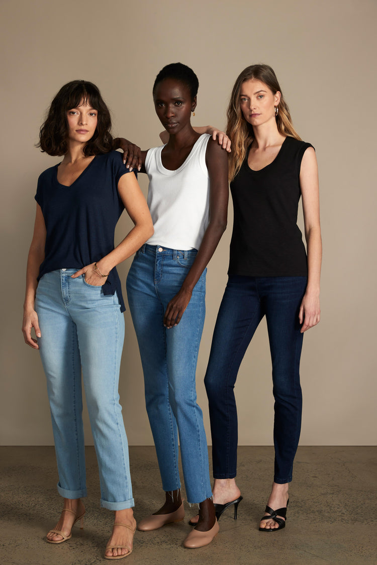 Three women model assorted basic cotton sleeveless tops in black, white, and navy, paired with straight and slim blue jeans.