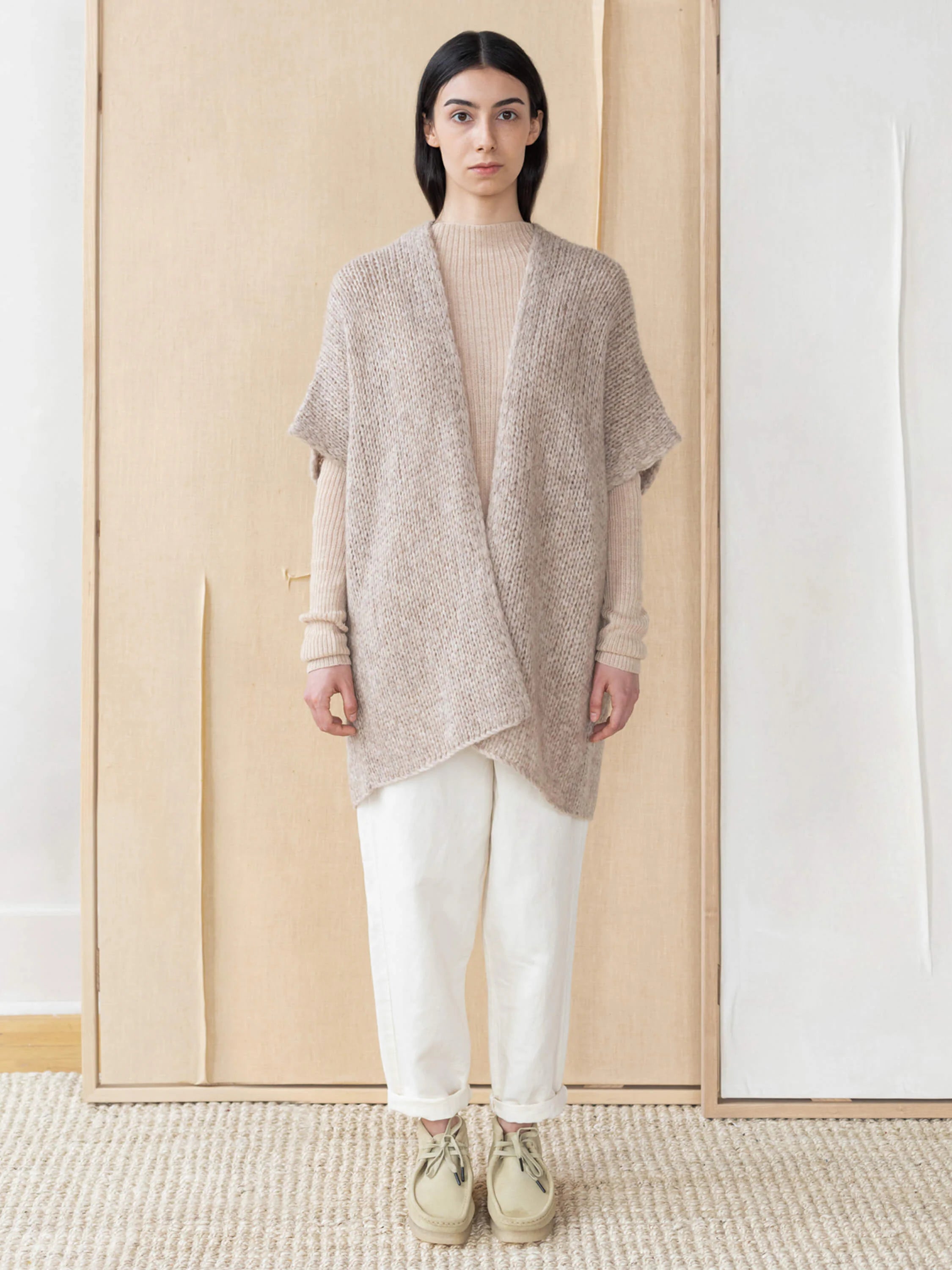 Beige knitted vest; open front, short sleeves. Model wears it over a lighter beige top.