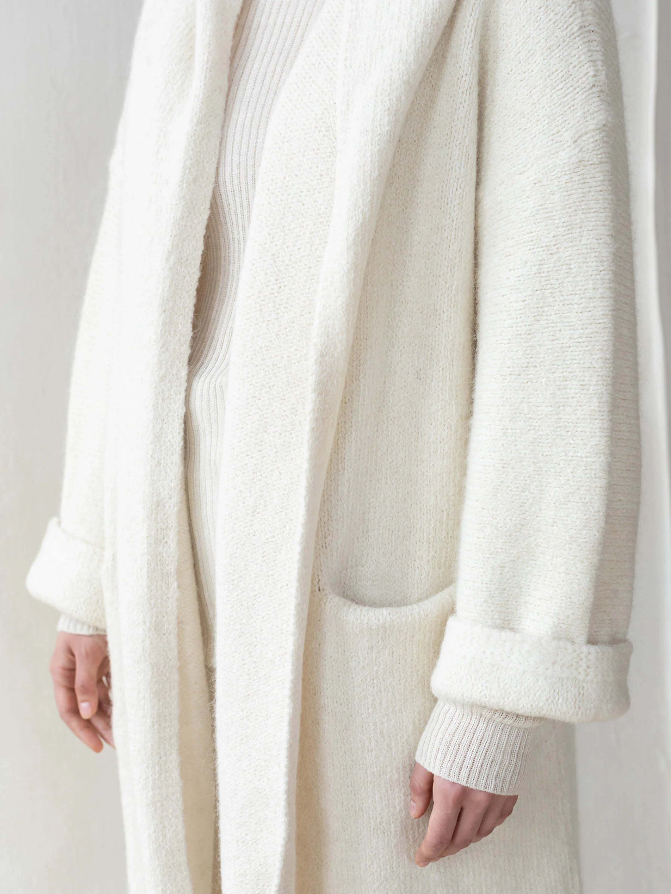 Off-white alpaca hooded coat. Long sleeves, pockets, and a relaxed fit. Knitted texture.
