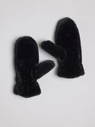Pair of black faux fur mittens, fluffy texture, standard mitten shape with separate thumb, on light background.