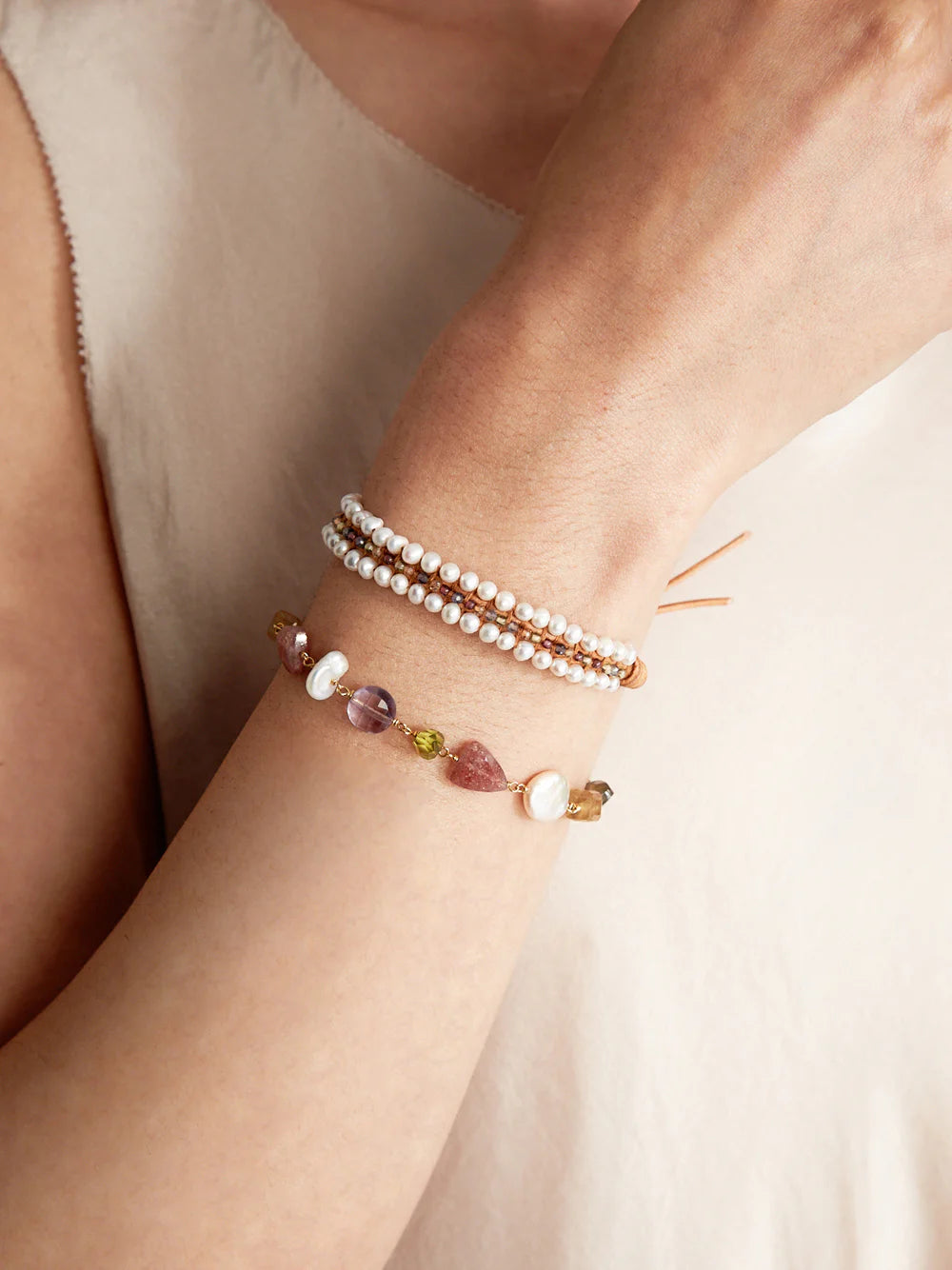 Two bracelets on wrist. Top: pearls, small brown & white beads, tan leather cord. Bottom: pink, purple, green stones,...