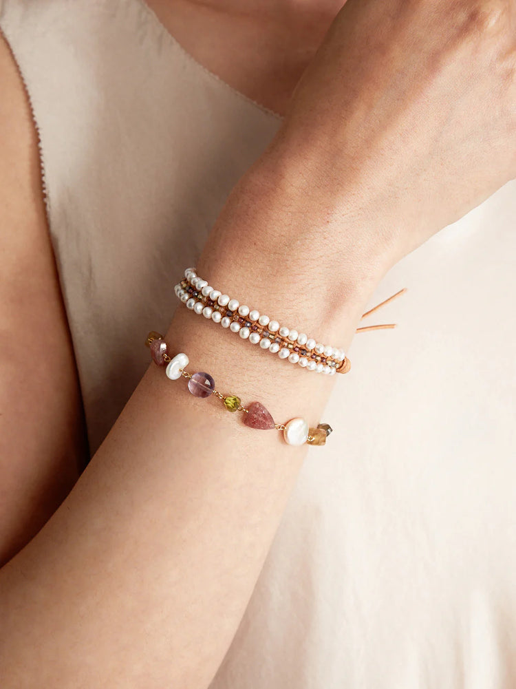 Two bracelets on wrist. Top: pearls, small brown & white beads, tan leather cord. Bottom: pink, purple, green stones,...