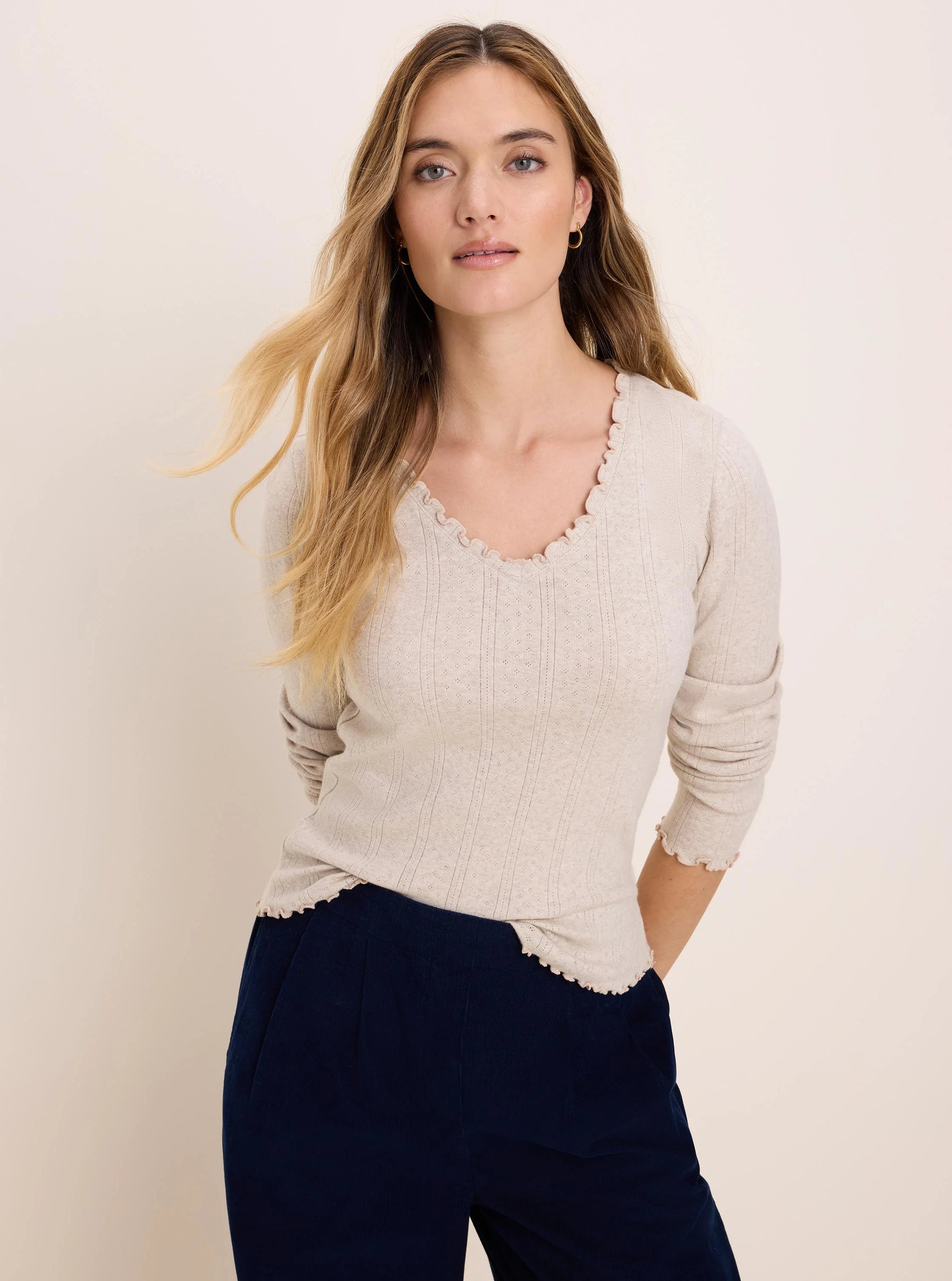Light beige pointelle rib long sleeve tee with a V-neck and ruffled trim on neckline, cuffs, and hem.