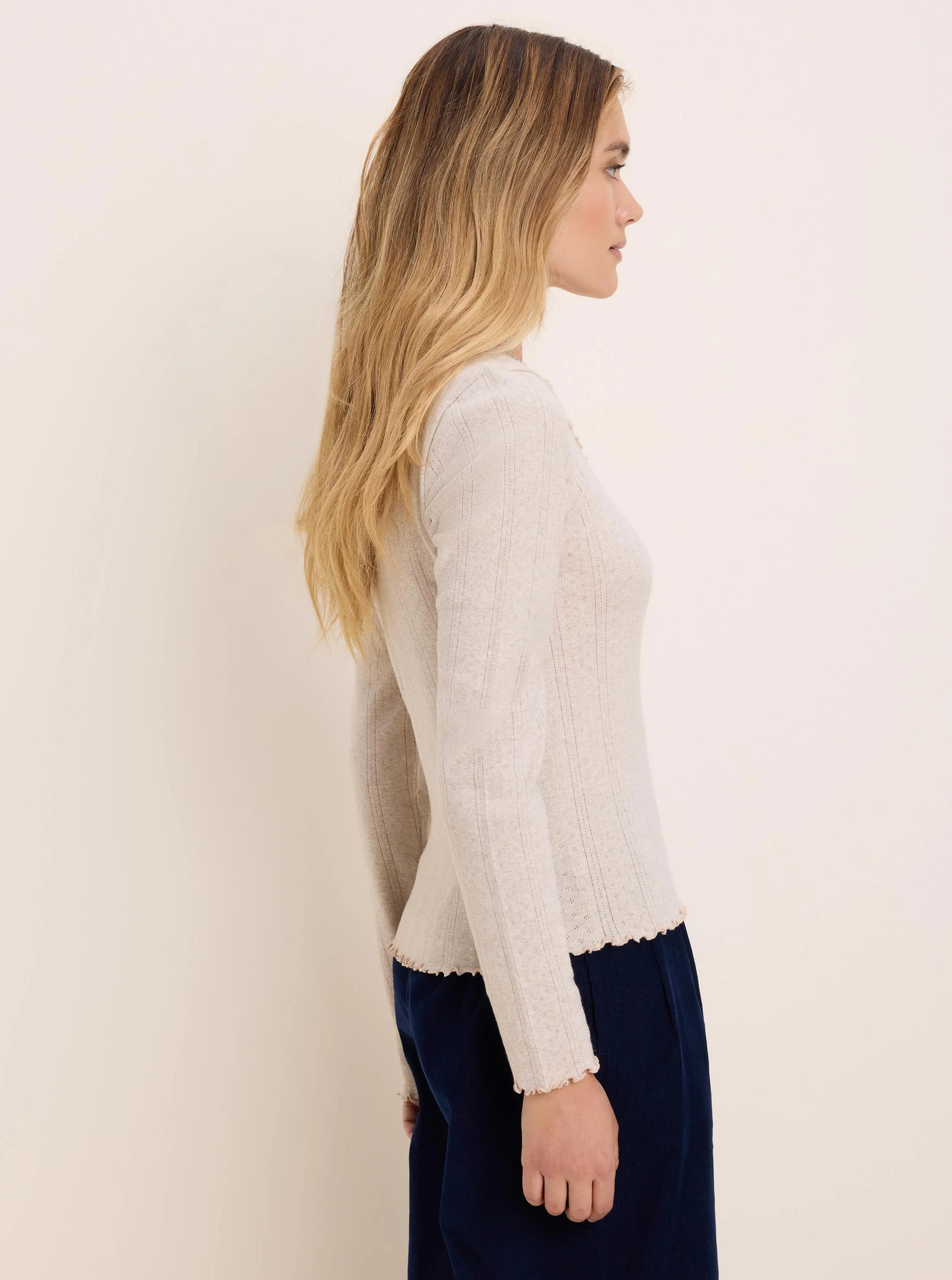 Light beige pointelle rib long-sleeve tee with fine textured lines and ruffled cuffs and hem.
