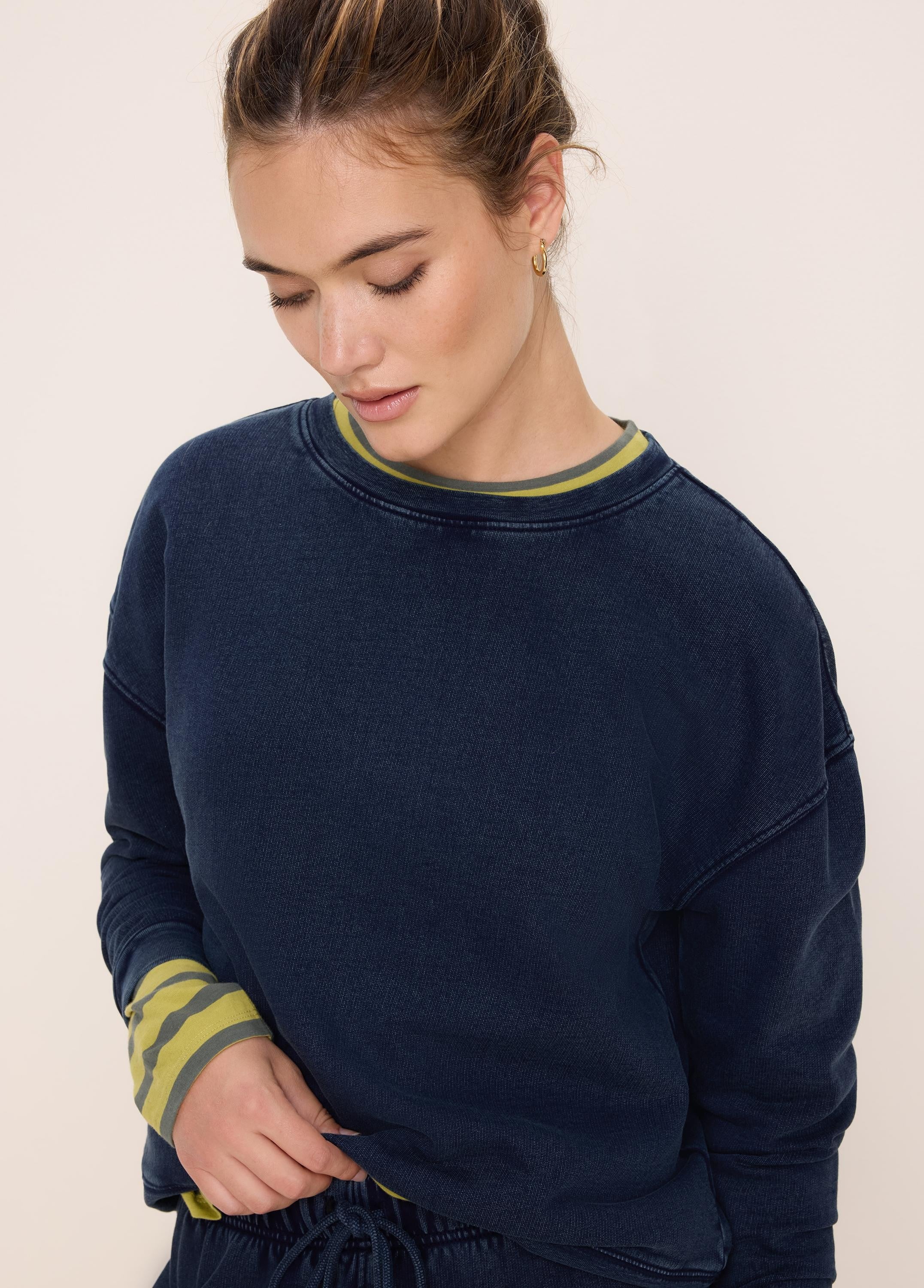 Navy cotton terry crewneck sweatshirt. A striped yellow and grey long-sleeve shirt is visible at the neck and cuffs.