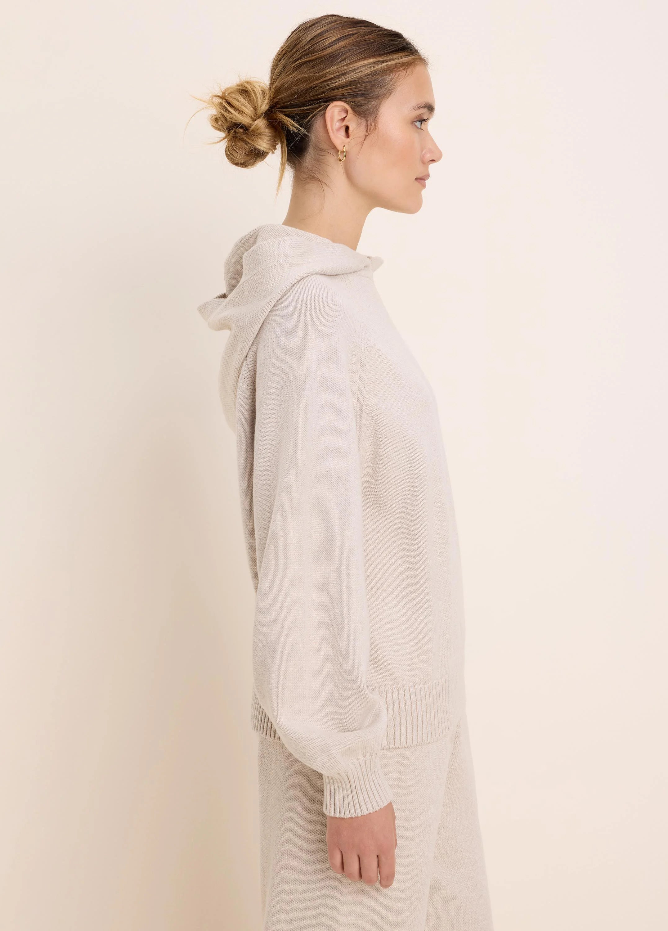 Light beige knit sweater hoodie with a hood and ribbed cuffs and hem, shown on a model in profile.