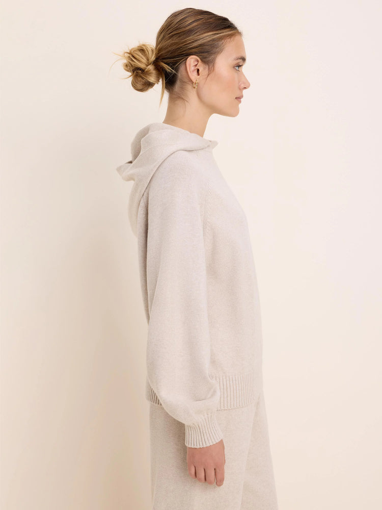 Light beige knit sweater hoodie with a hood and ribbed cuffs and hem, shown on a model in profile.