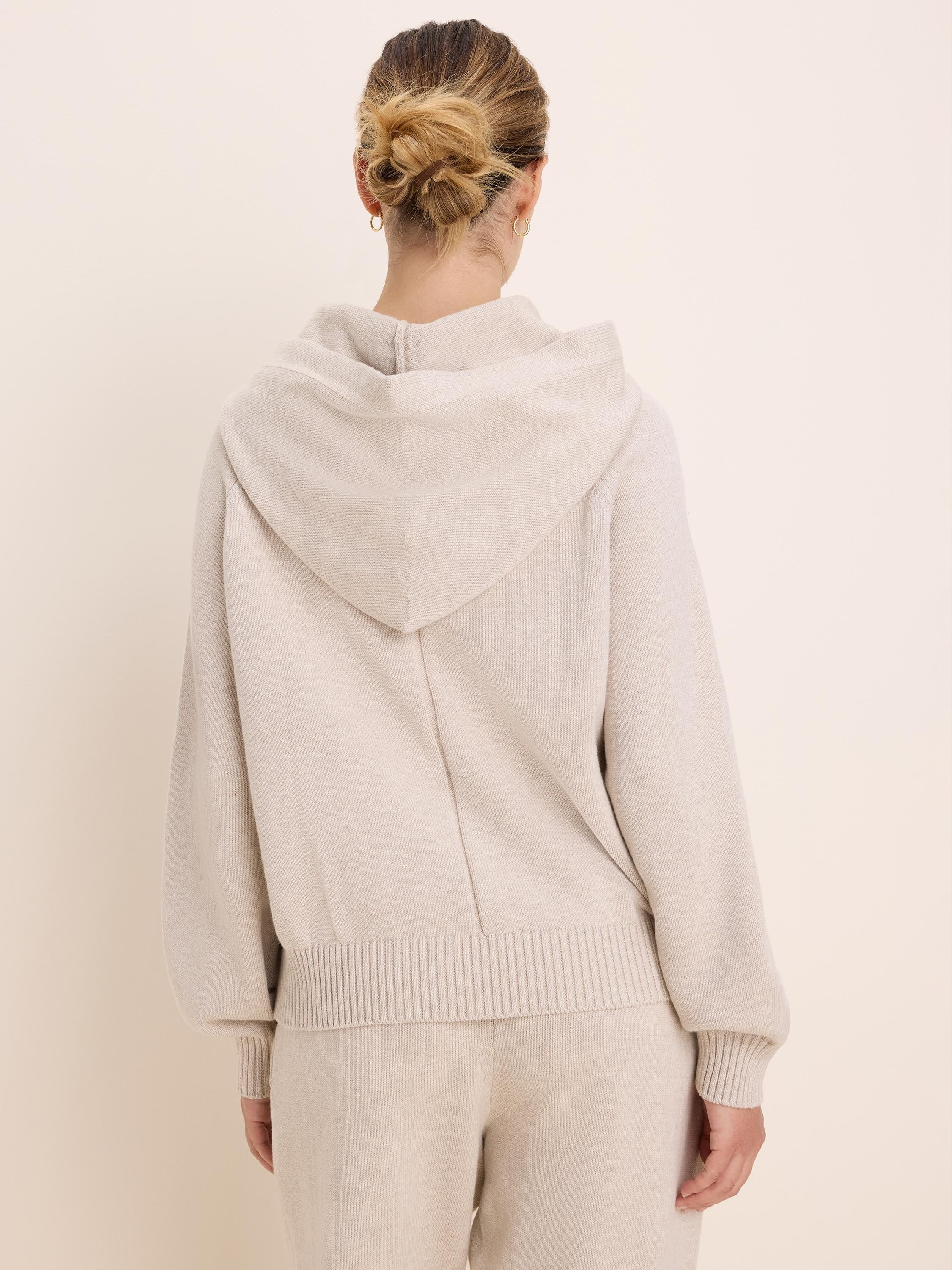 Loose-fitting light beige knit sweater hoodie with a hood, ribbed cuffs, and hem. Model shown from the back.