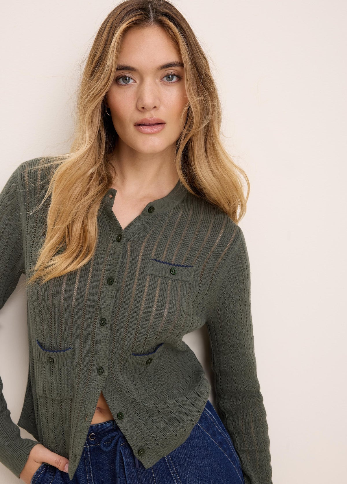 Olive green pointelle knit cardigan with button front and two blue-trimmed chest pockets.