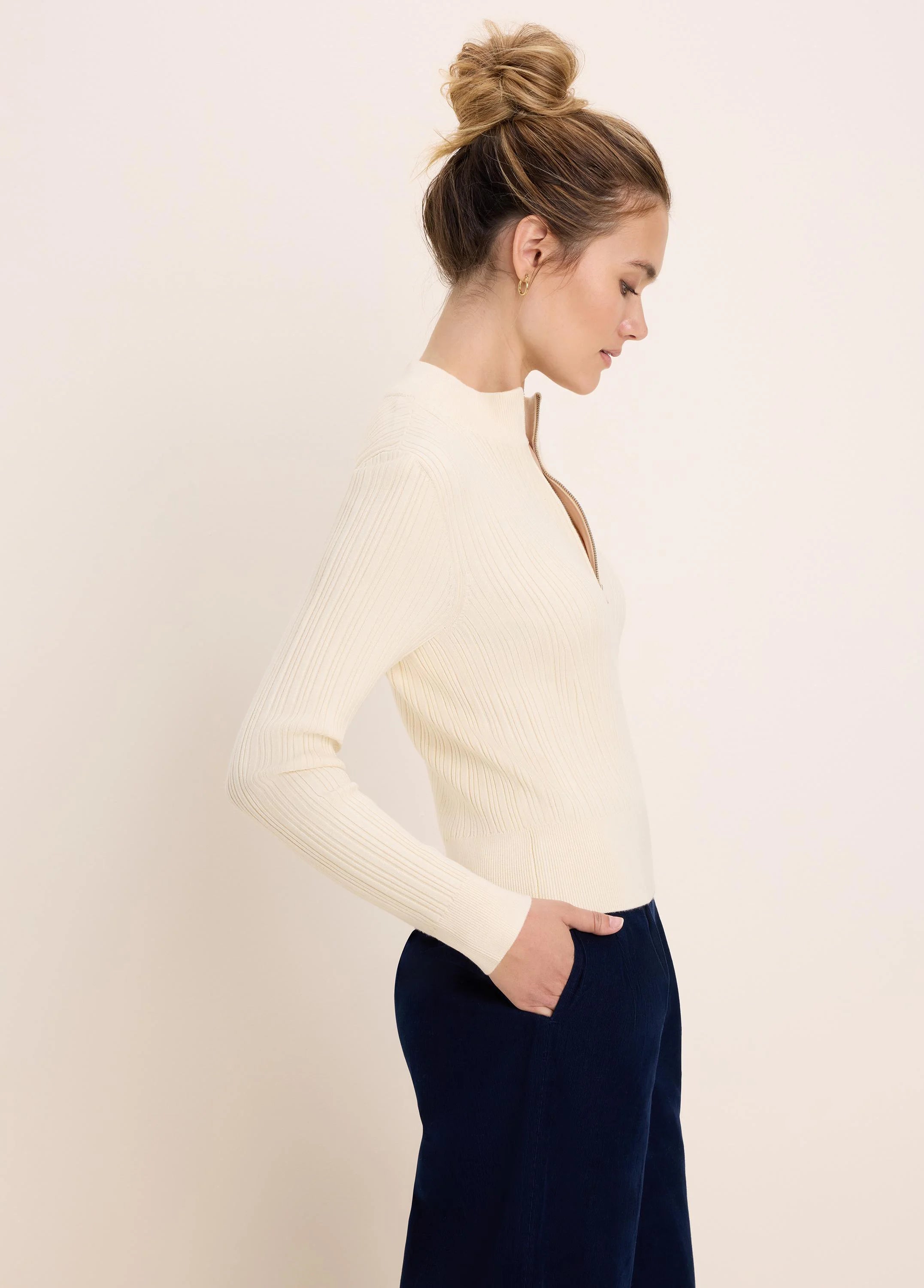 Cream ribbed half-zip sweater with a gold zipper partially open, mock neck.