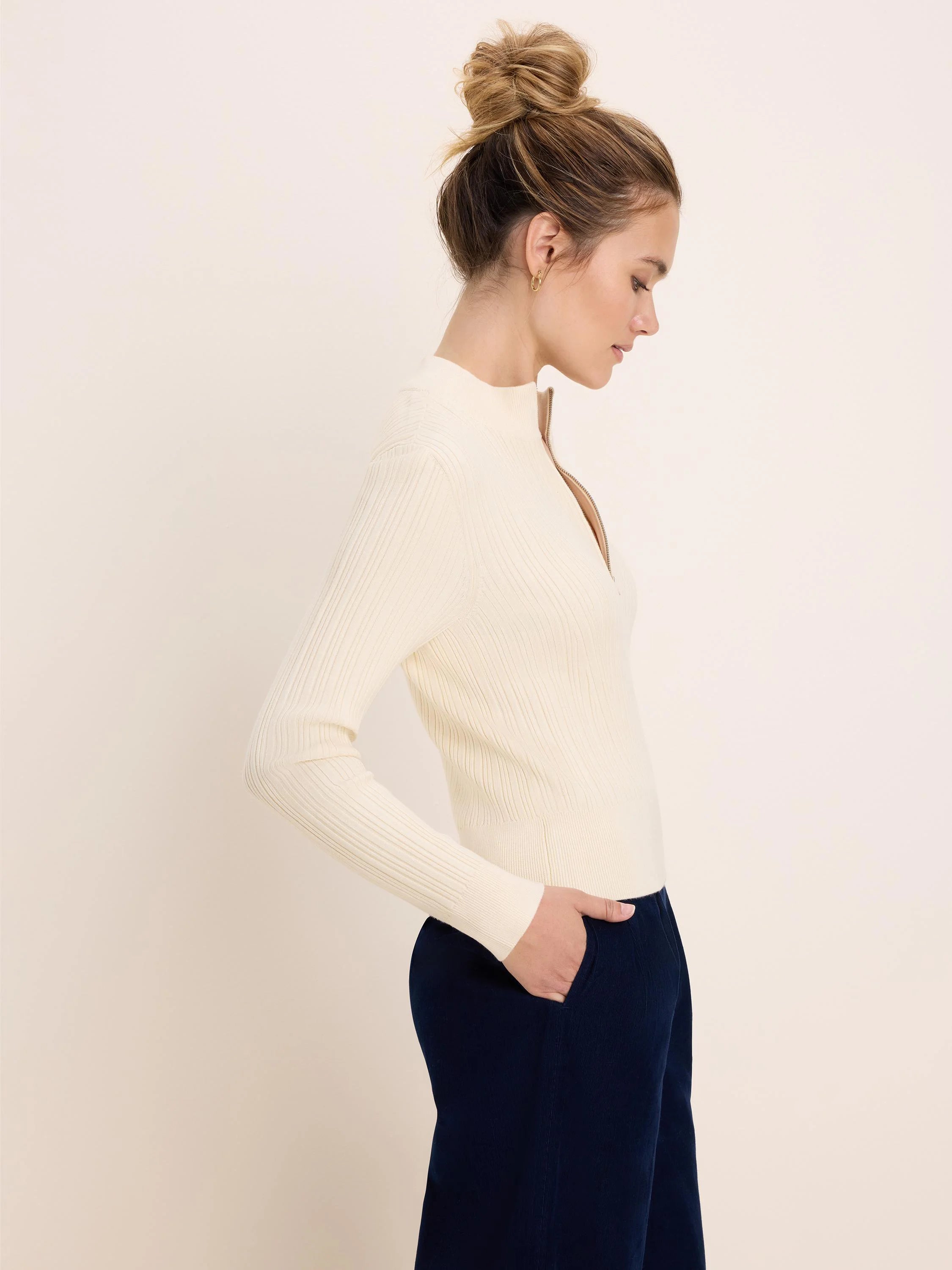 Cream ribbed half-zip sweater with a gold zipper partially open, mock neck.