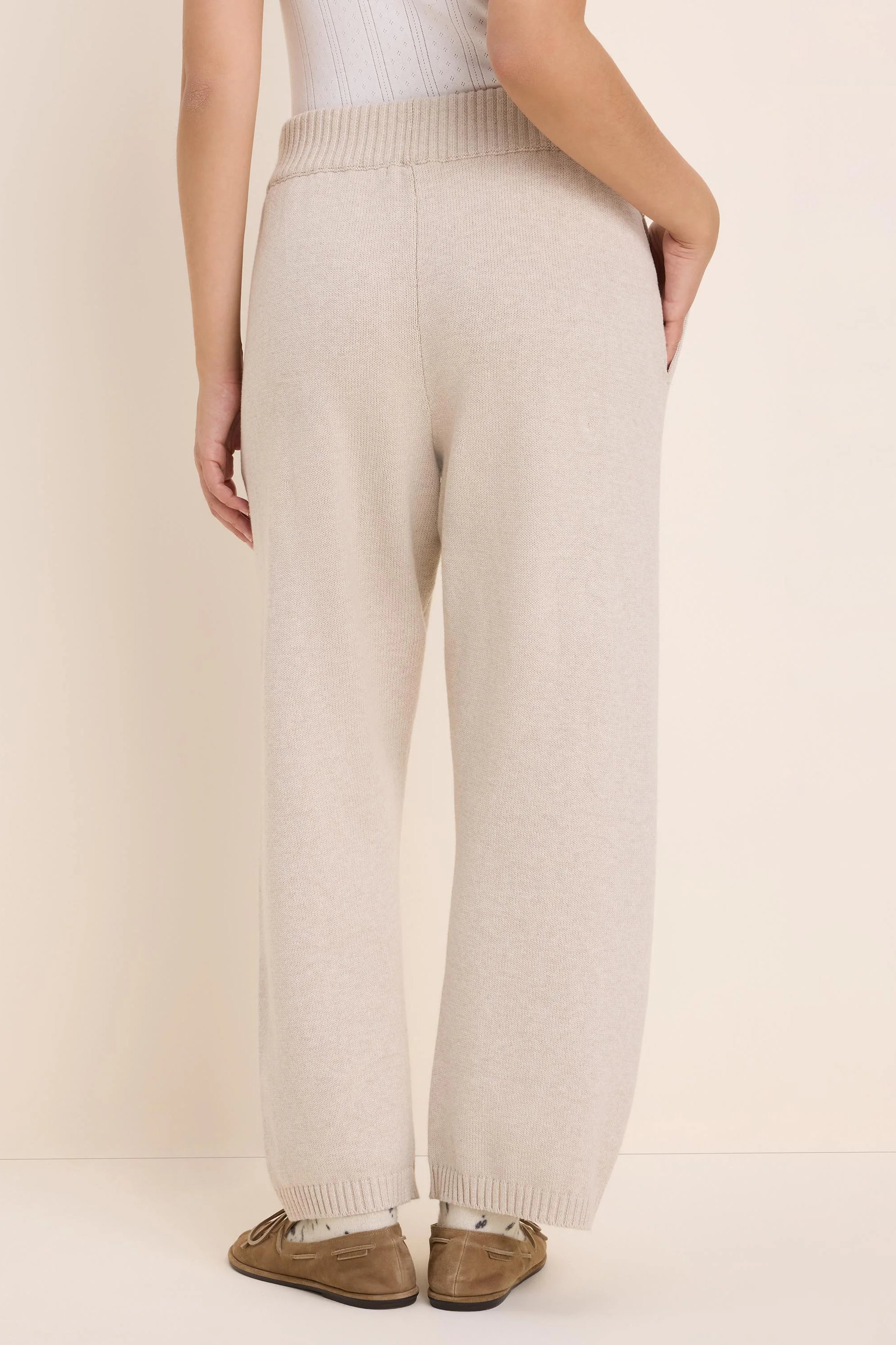 Light beige wide-leg knit pants with ribbed waistband and cuffs, shown from the back.