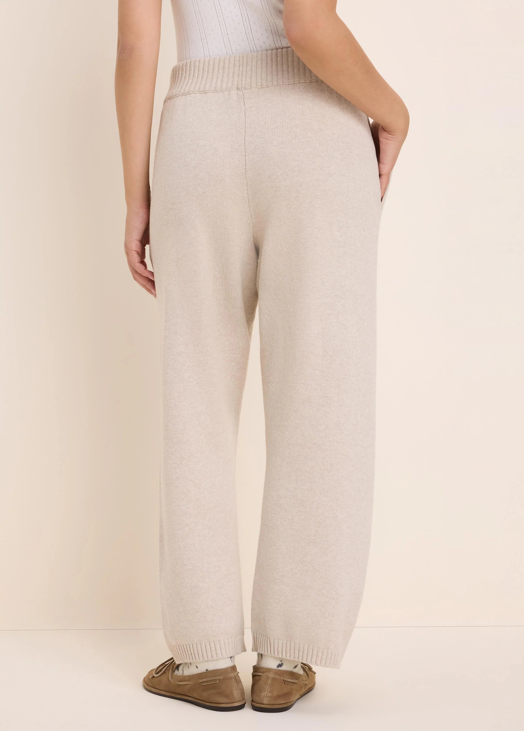 Light beige wide-leg knit pants with ribbed waistband and cuffs, shown from the back.
