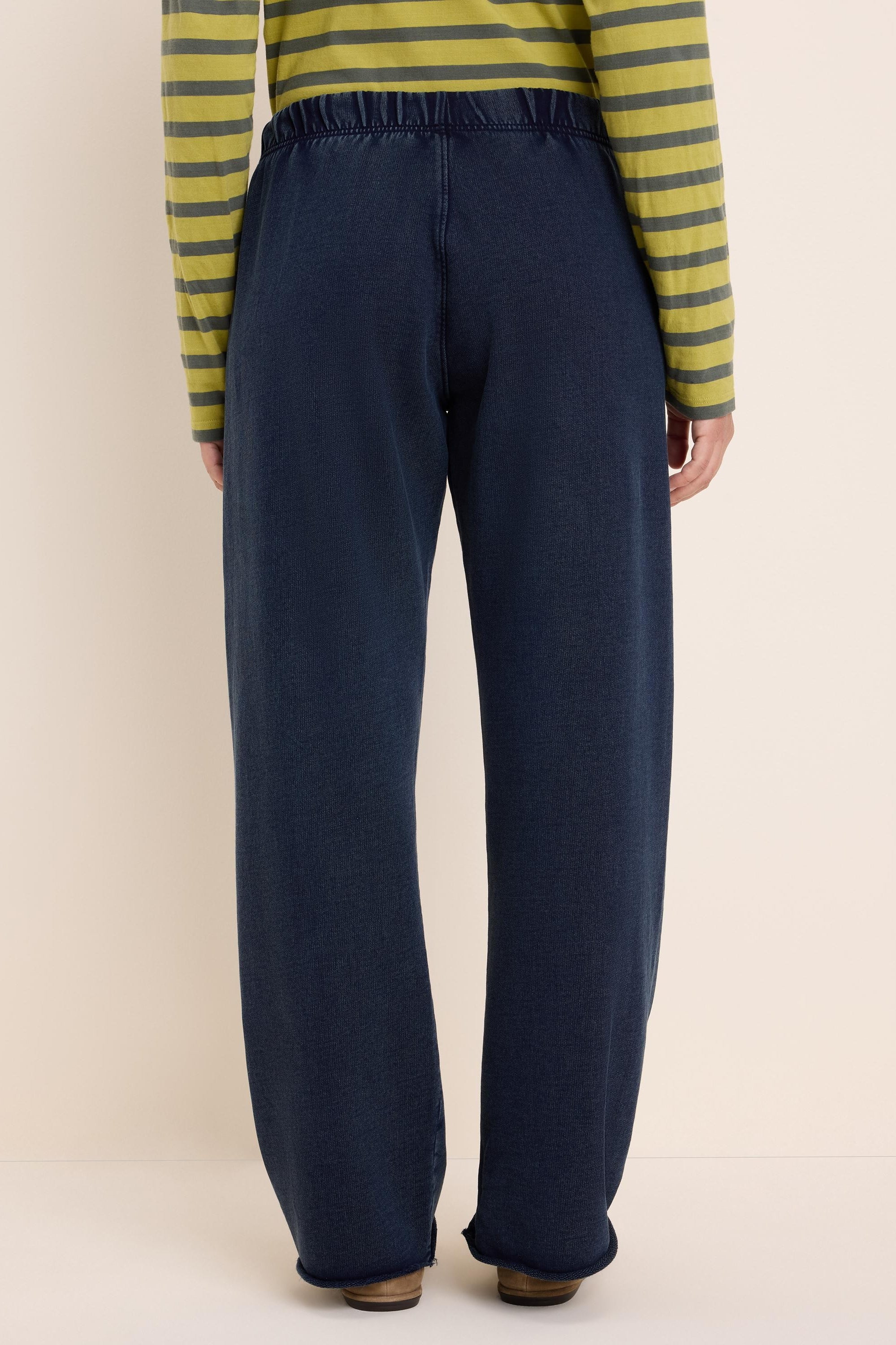 Dark blue relaxed-fit pants with wide straight legs, an elasticated waist, and an unfinished hem. Back view.