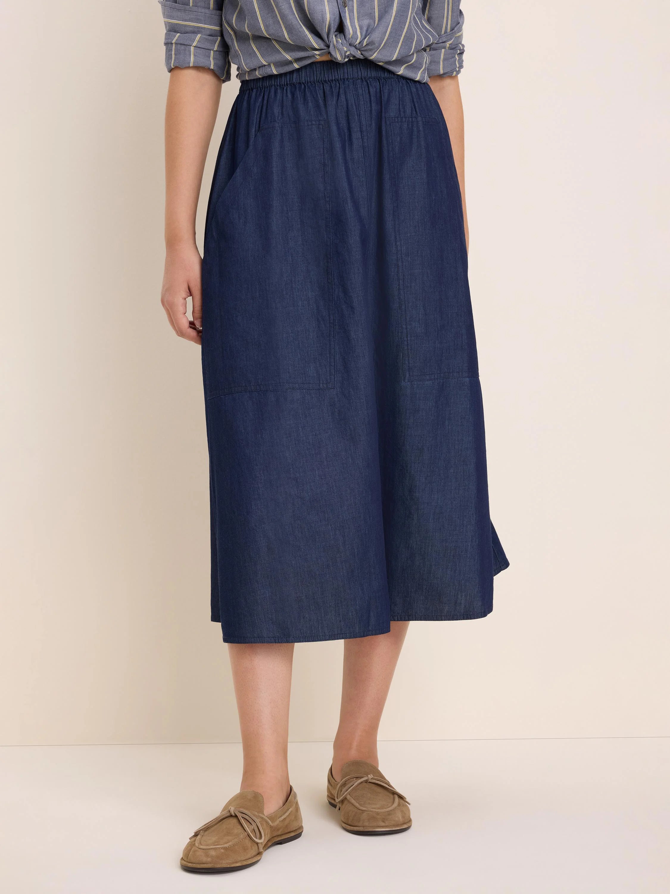 Dark blue denim midi skirt with elastic waist, two front patch pockets, and a drapey A-line shape.