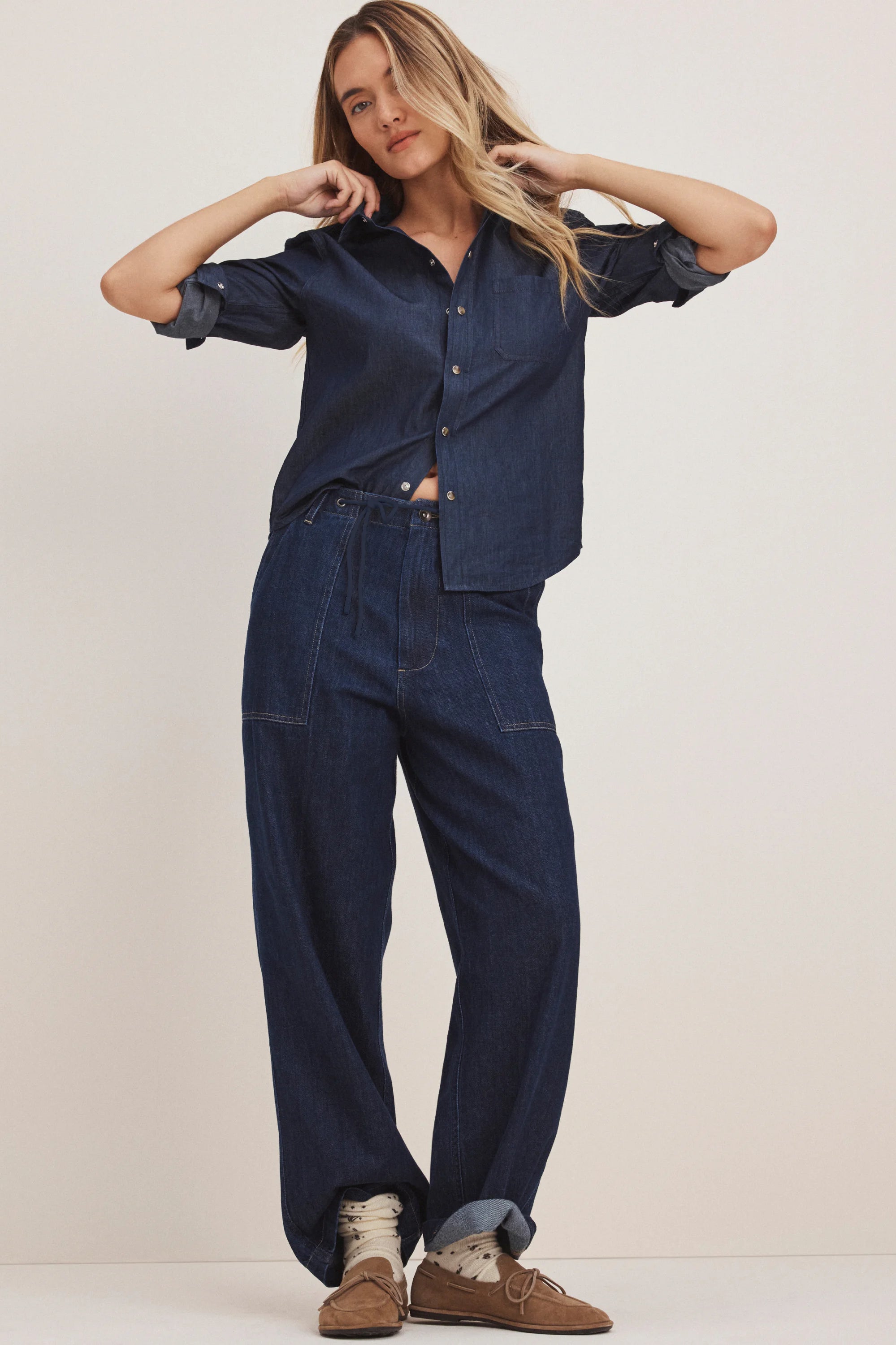 Dark blue wide-leg denim pants with a drawstring waist, prominent front patch pockets, and rolled-up cuffs.