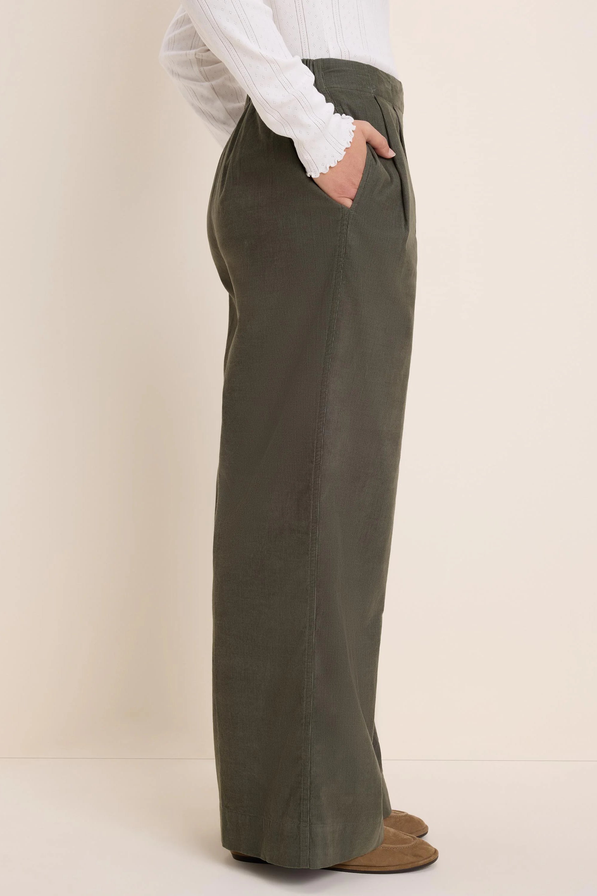 Dark olive green baby corduroy wide-leg pants with pleated waist. Model's hand in one front pocket.