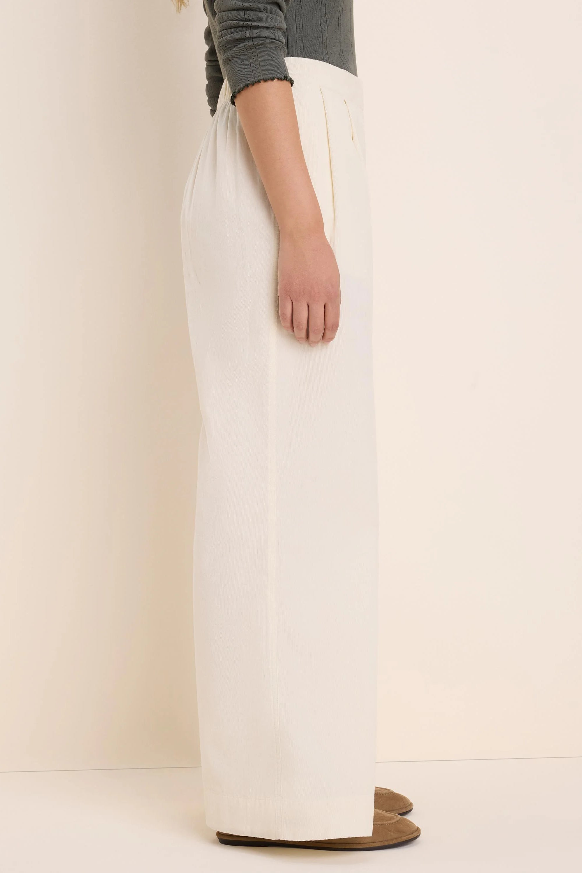 Cream baby cord wide-leg pants with front pleats, shown from the side on a model.