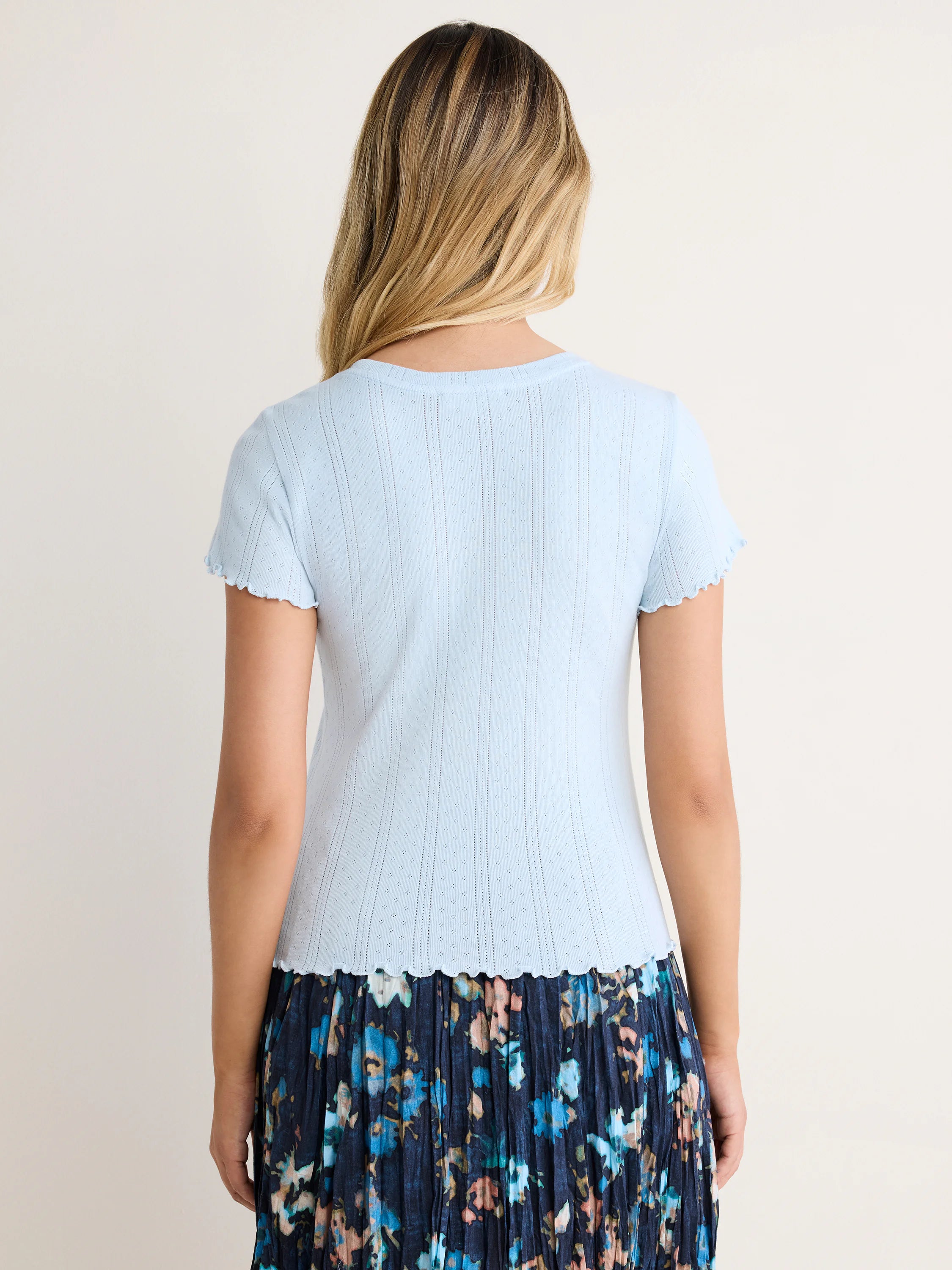 Back view of a light blue tee. Features fine vertical ribbing & small openwork dots, crew neck, and scalloped short sleeves.