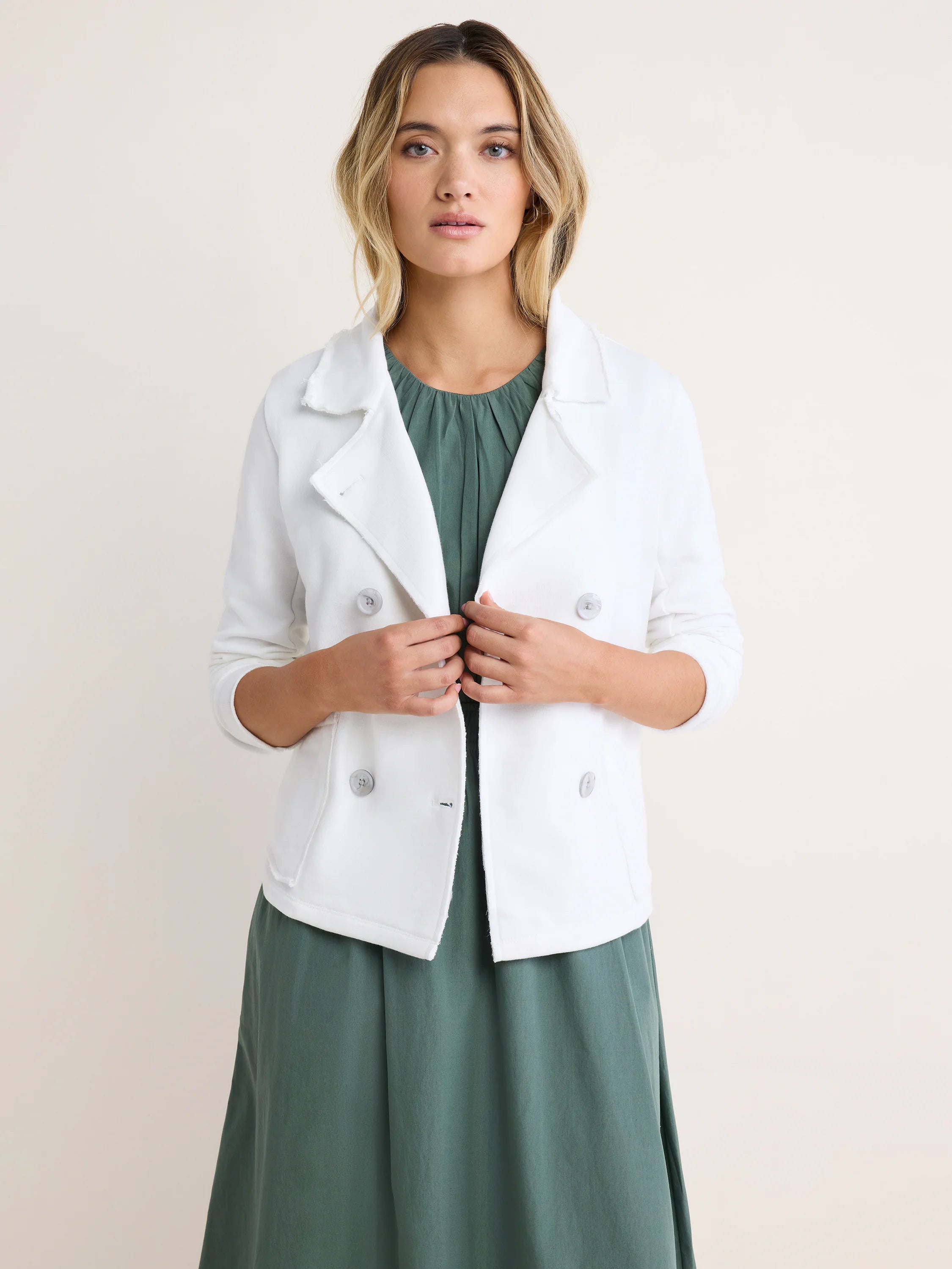 White French Terry Daily Jacket with double-breasted front, frayed lapels, and clear buttons. Worn open over a green dress.