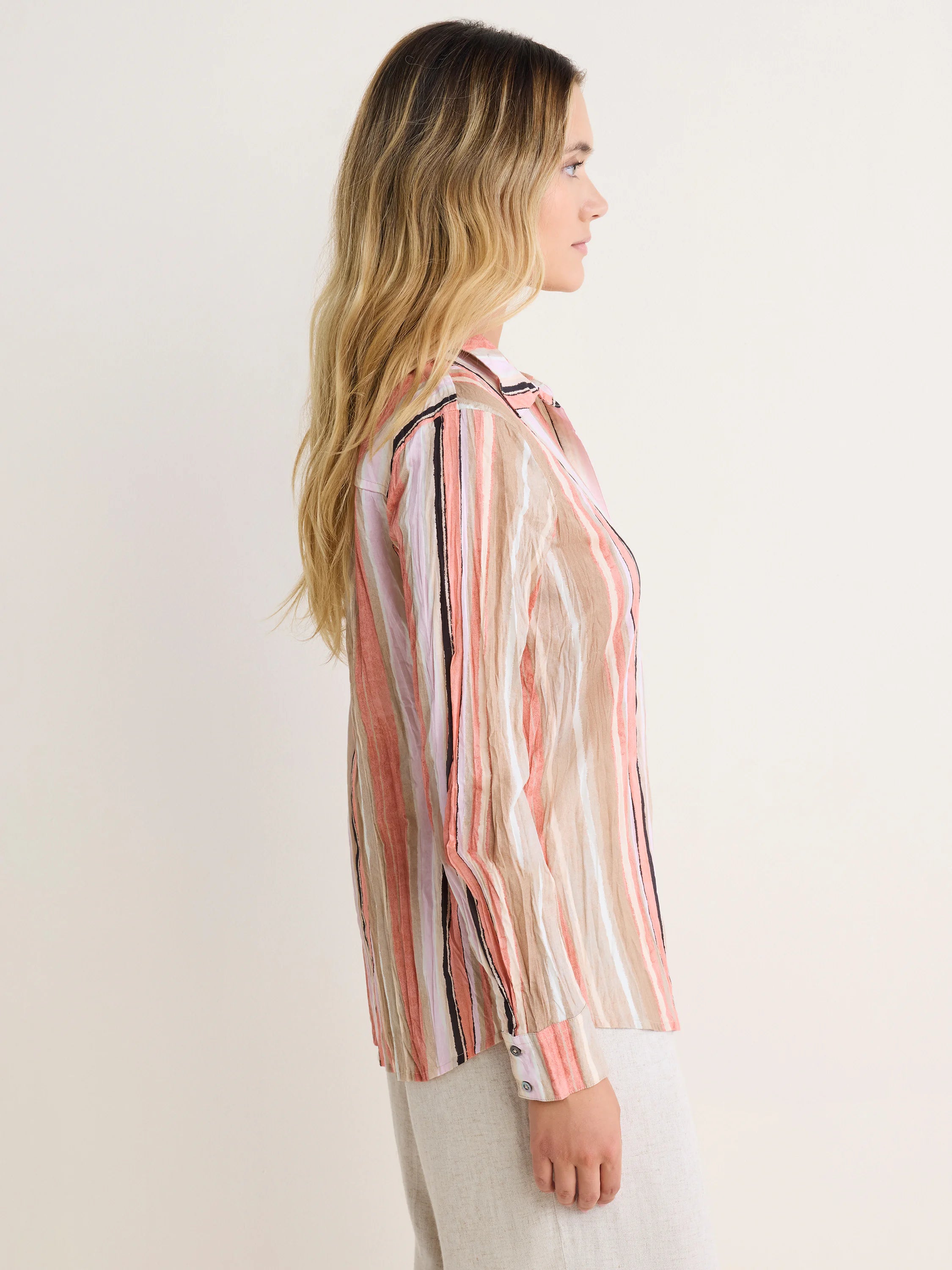 Striped cotton shirt with vertical peach, tan, white, lavender, black crinkled stripes. Model's side view.