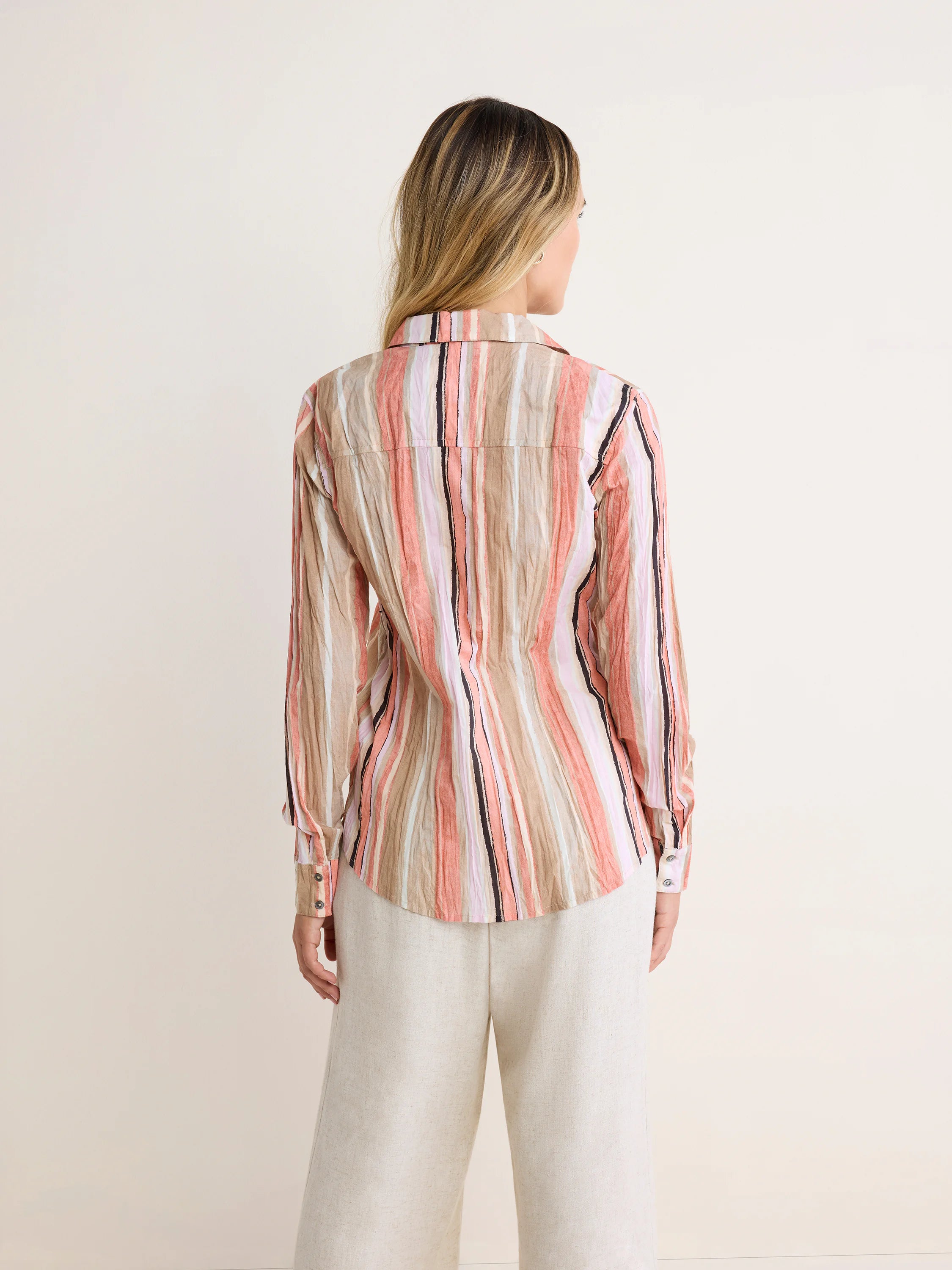 Crinkled shirt with vertical stripes in tan, light pink, white, and black. Model wears from back.