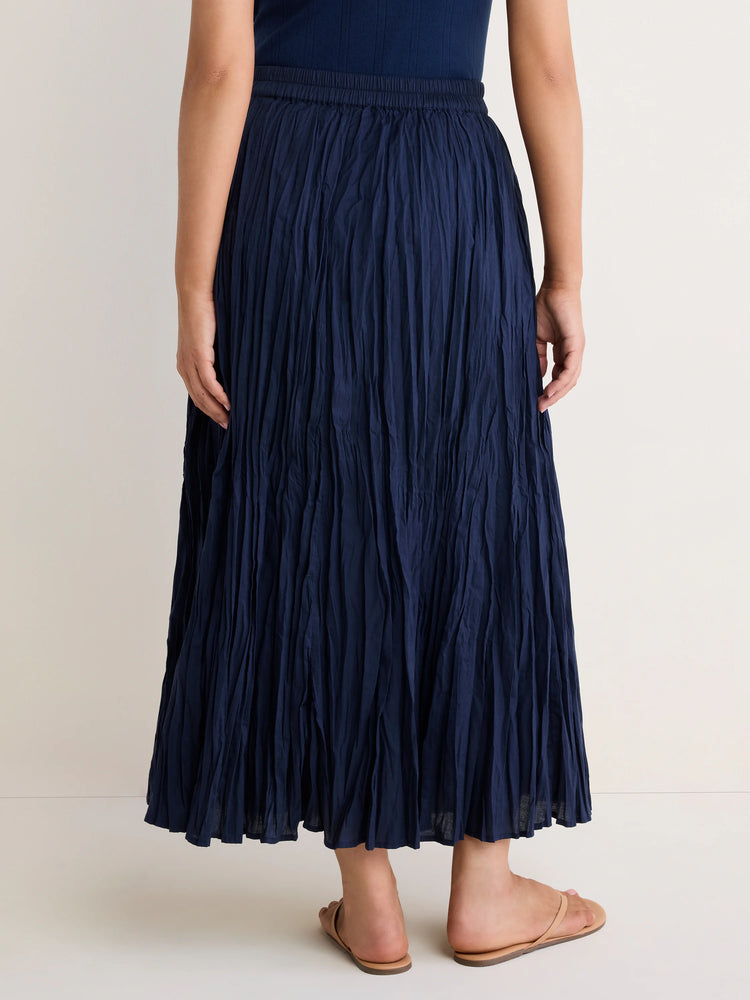 Dark blue cotton crinkle maxi skirt with prominent vertical texture & elastic waist, worn by a model from behind.