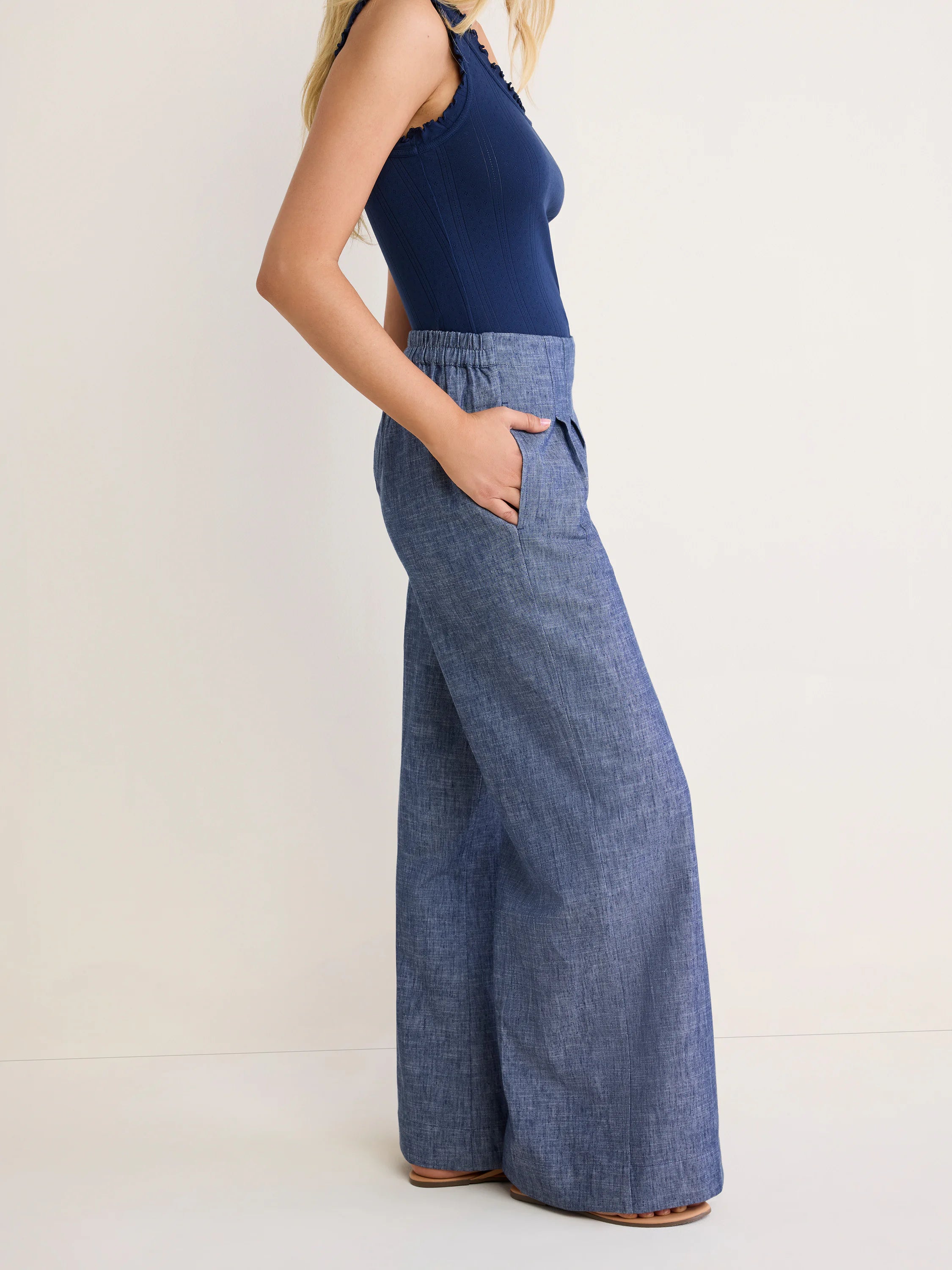 Ellis Trouser in medium blue chambray on model. Features wide-leg, full-length cut, gathered elastic waist, and side pockets.
