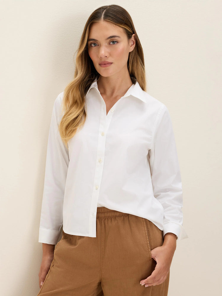 White collared stretch cotton shirt with light-colored buttons and cuffed long sleeves, worn untucked.