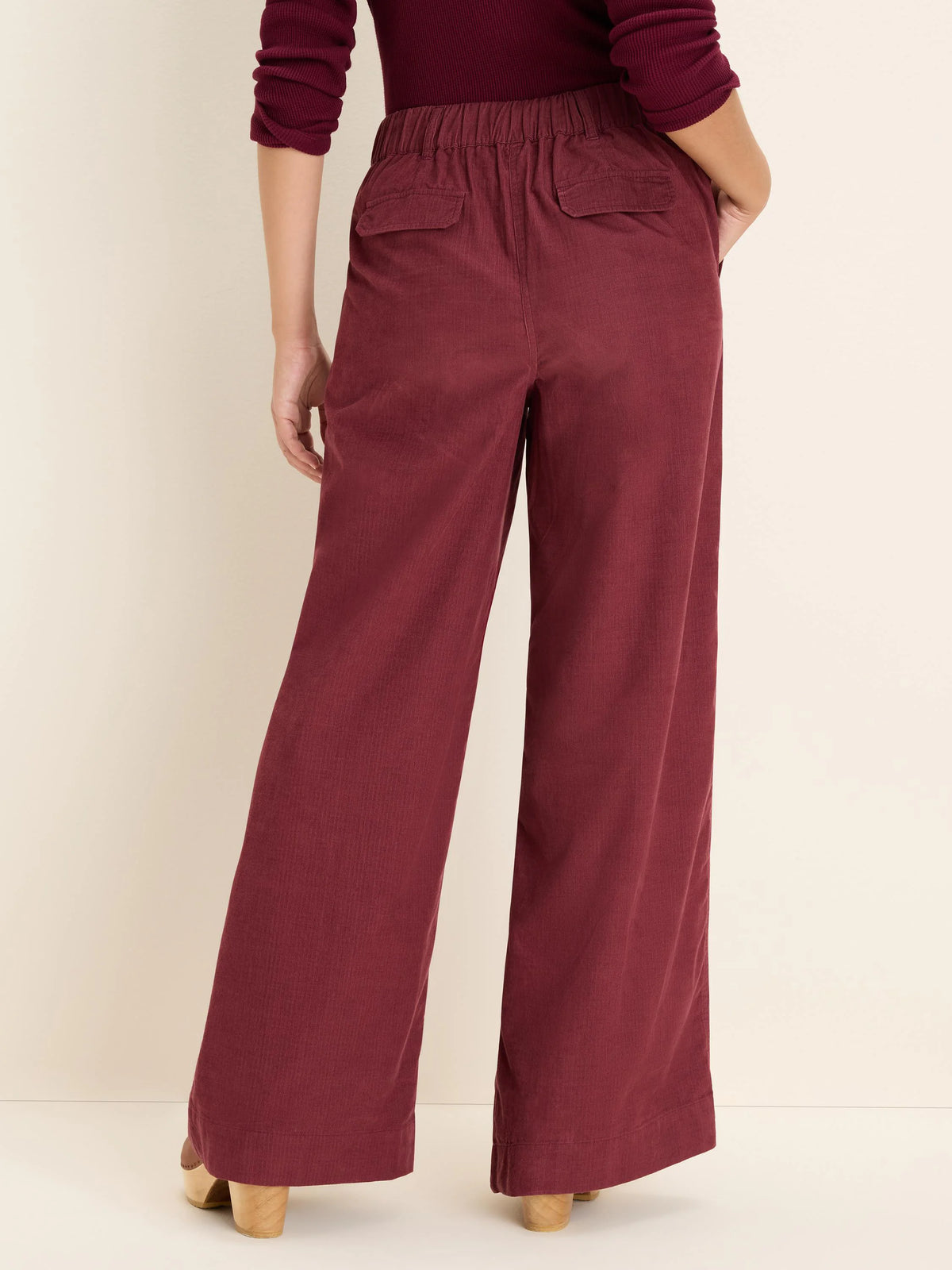 Dark red wide-leg corduroy pants. Features an elastic waist, and two back flap pockets. Back view.