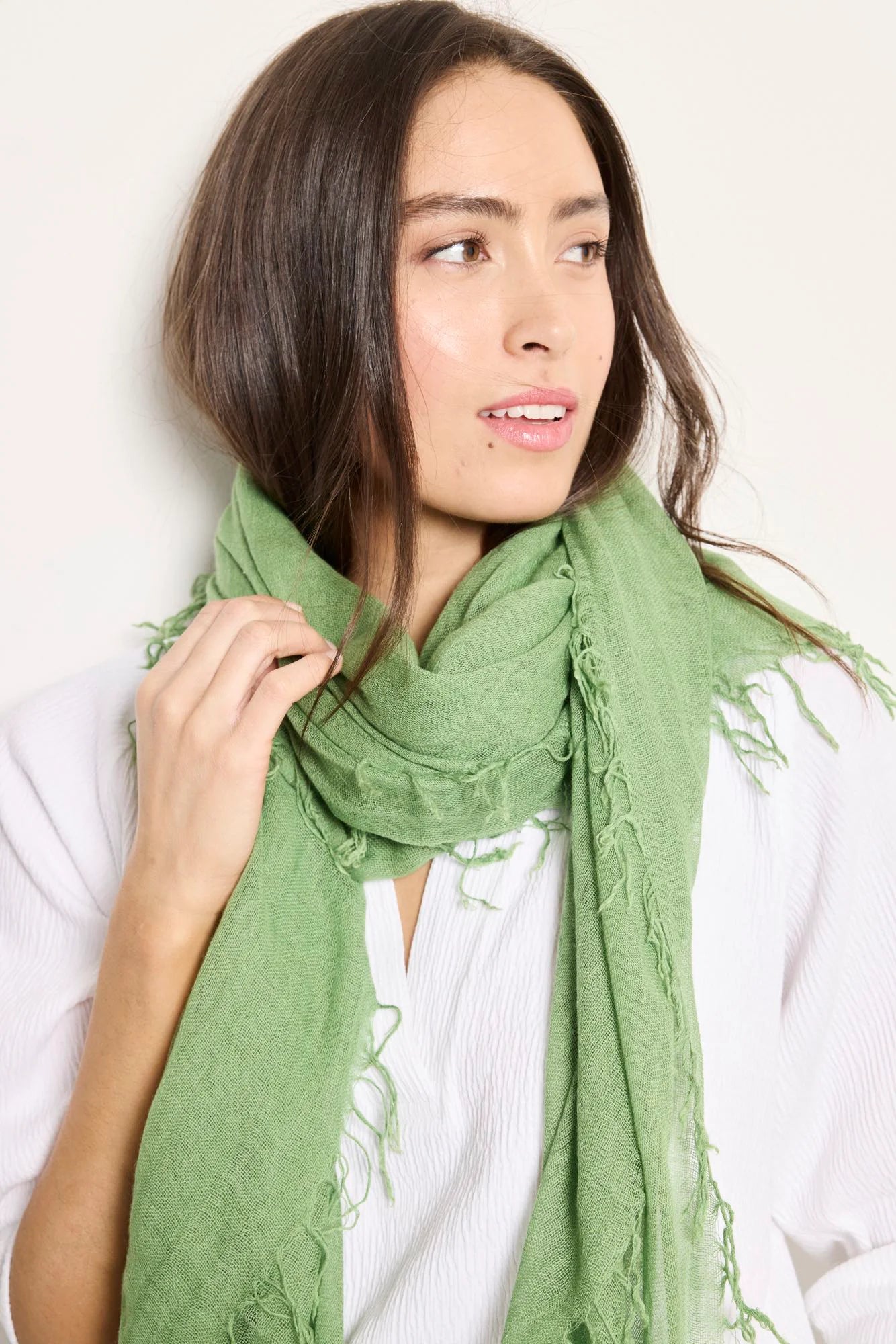 Sage green rectangular scarf with frayed edges. Model is wearing it loosely around neck.