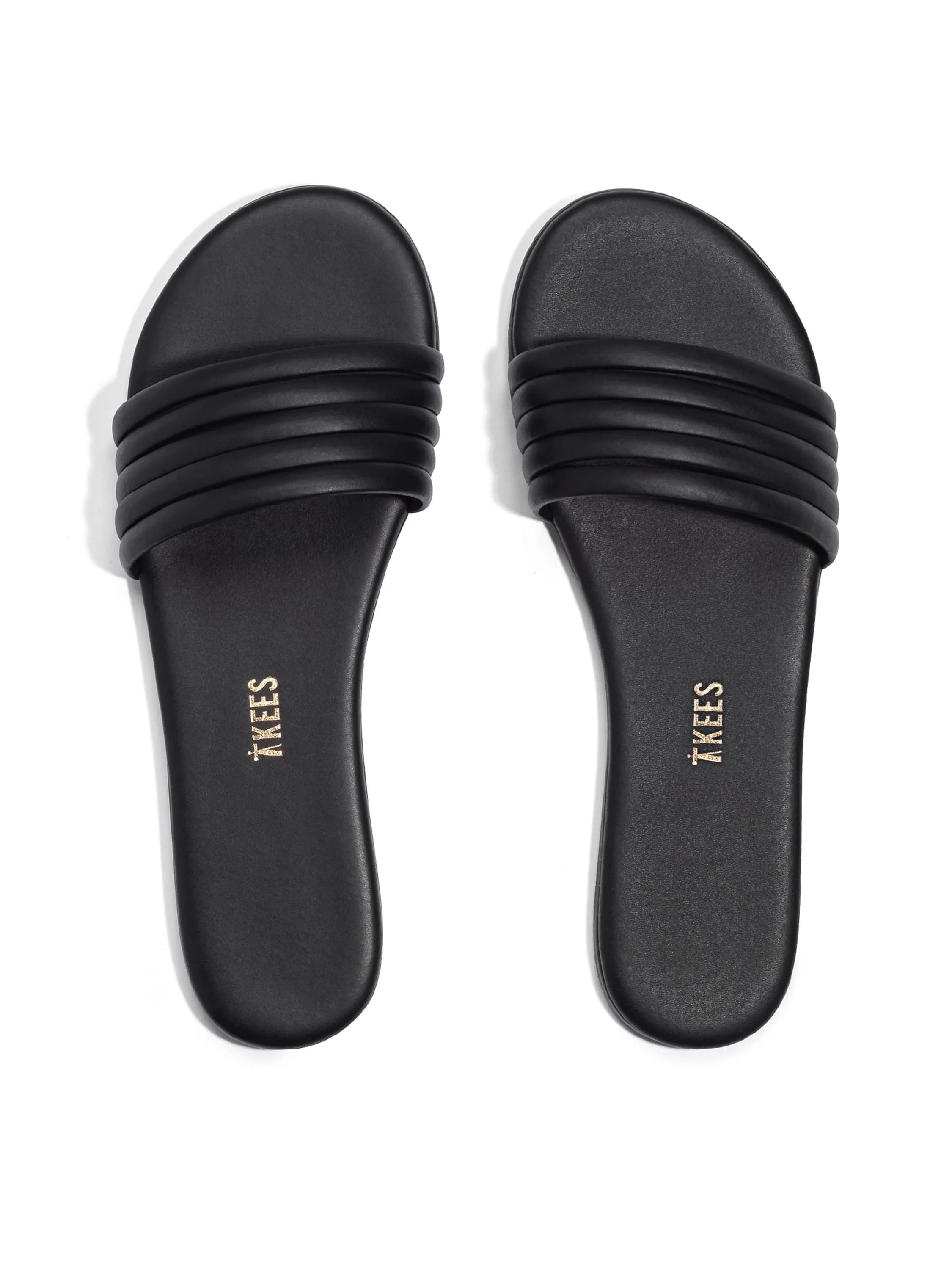 Black leather slides with three horizontal bands across the top.  "TKEES" is embossed on the soles in gold.