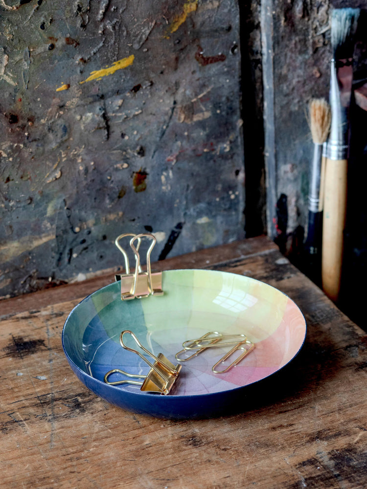 Round enamel tray; navy blue rim, pastel rainbow interior. Gold binder clips inside.