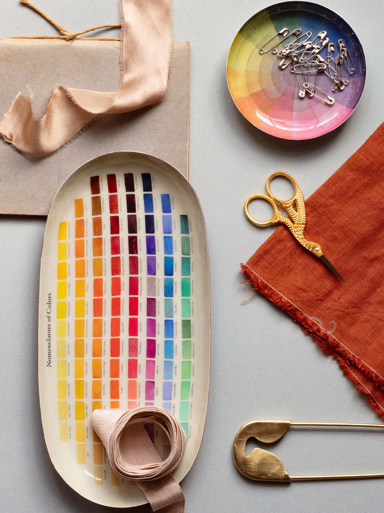 Oval enamel tray; white background with rows of colored paint swatches, from yellow to red to purple to blue and green.