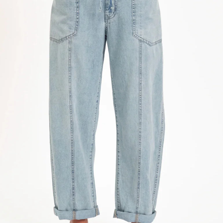 Light wash barrel leg jeans with a drawstring waist, large front patch pockets, front vertical seams, and cuffed hems.