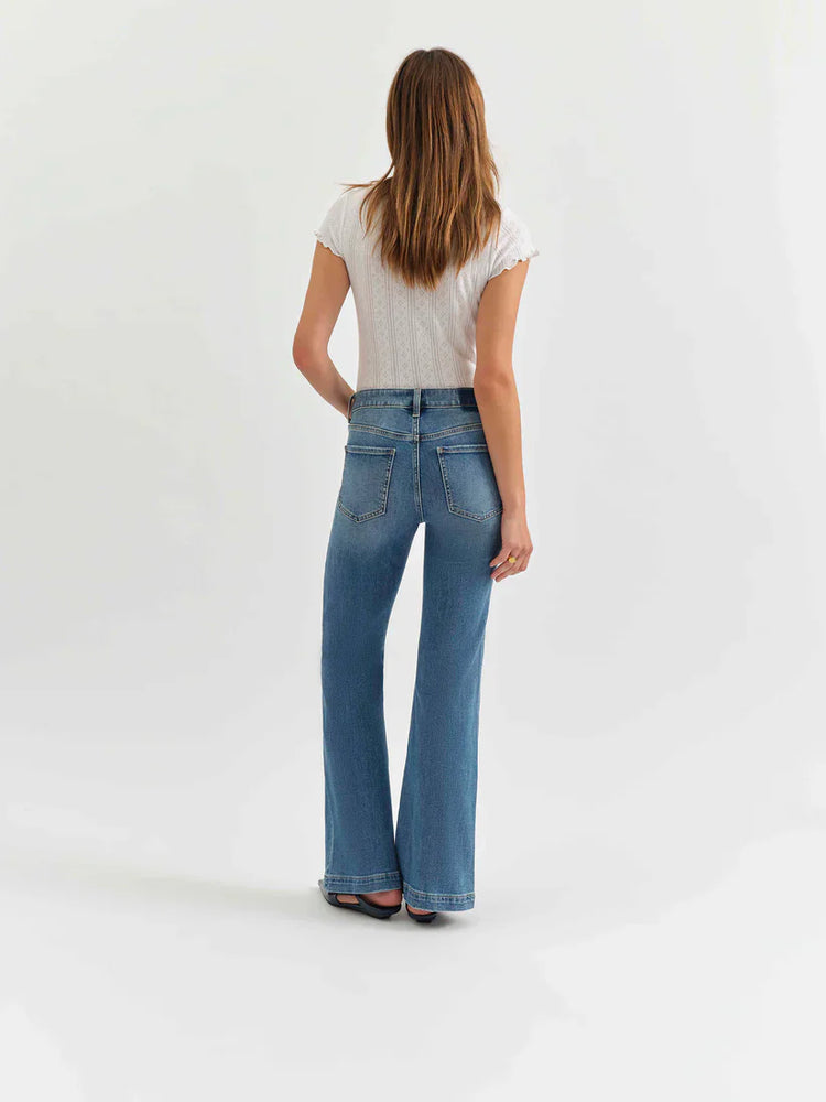 Rear view of model in medium blue mid-rise flare jeans. Fading on thighs, classic rear pockets, wide leg opening.