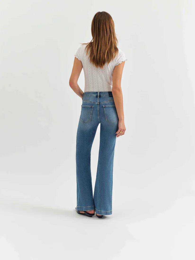 Rear view of model in medium blue mid-rise flare jeans. Fading on thighs, classic rear pockets, wide leg opening.