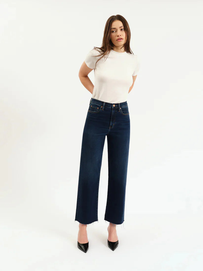 Dark wash, high-rise, wide-leg ankle jeans with a raw, frayed hem, shown on a model.