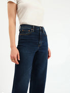 Dark blue high-rise wide ankle jeans, visible with yellow contrast stitching and copper rivets.
