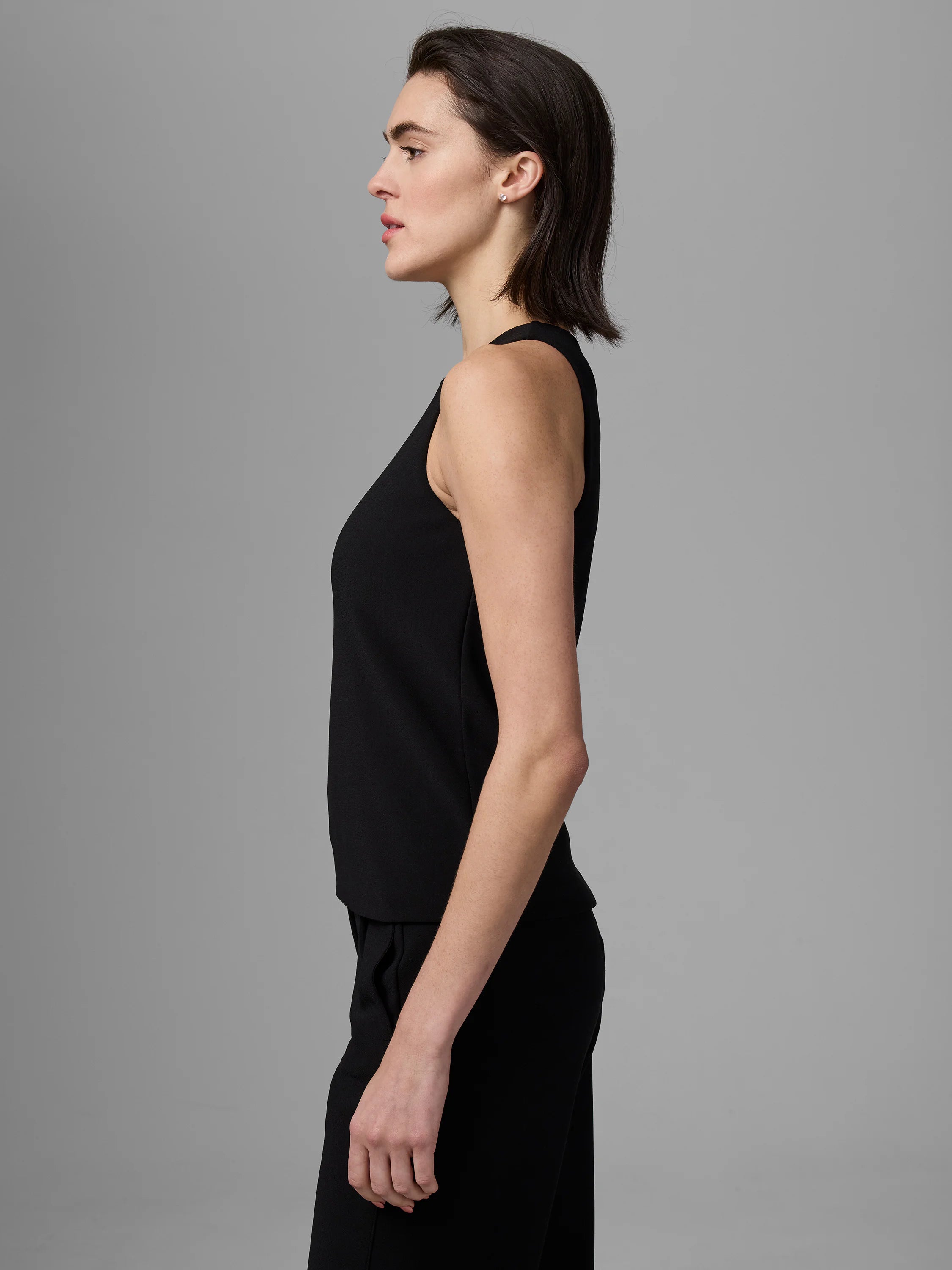 Black high-neck tank top on a model, shown in profile.