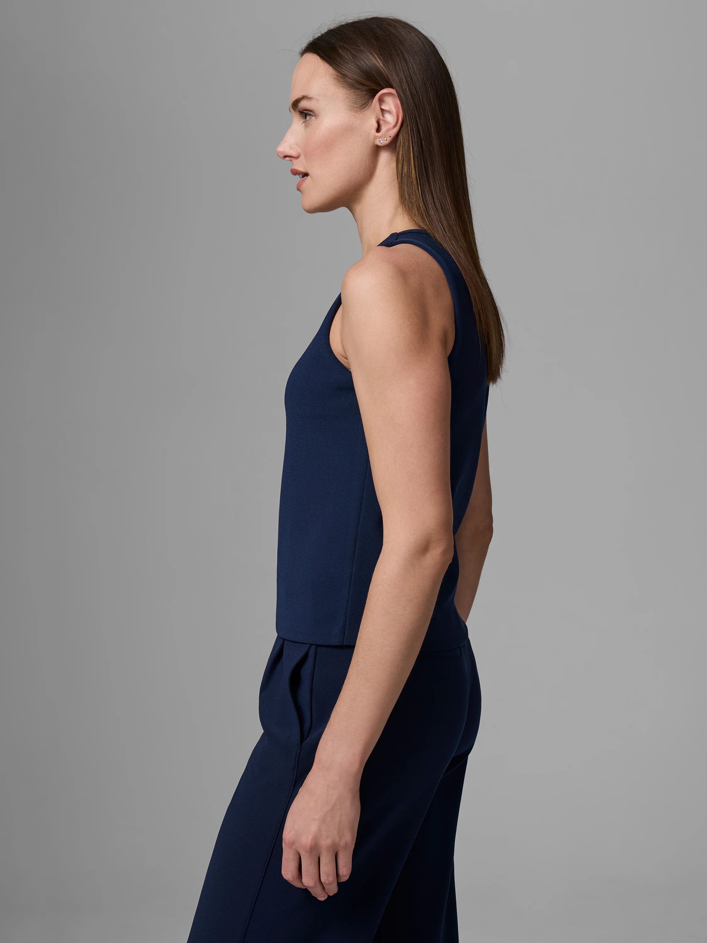 Navy knit scuba tank, sleeveless with a high, round neck, worn by a woman in side profile.