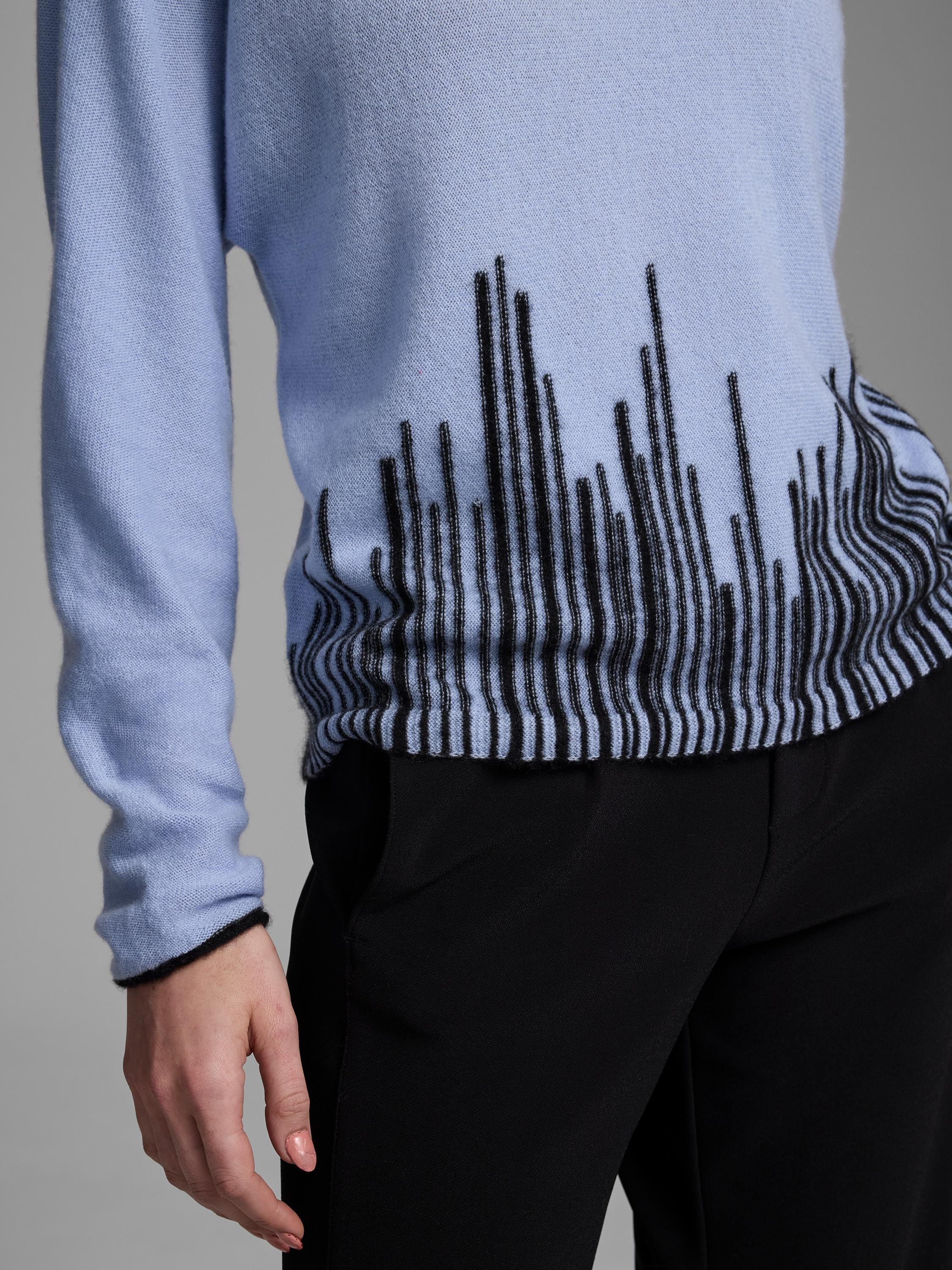 Light blue cashmere sweater with black vertical and wavy "flame stitch" pattern along the lower front and cuffs.