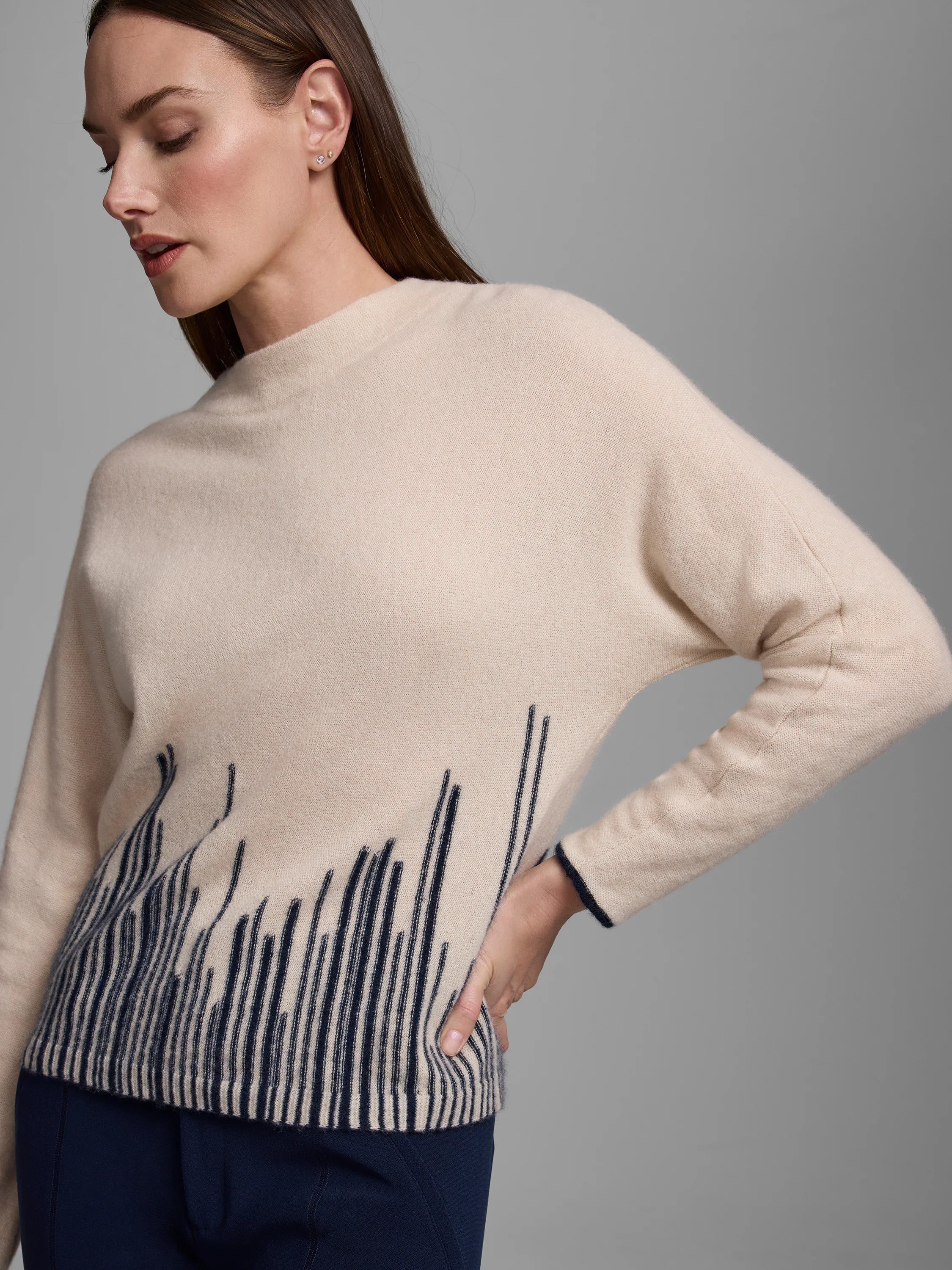 Light beige cashmere sweater featuring a dark blue flame stitch pattern rising from the bottom hem.