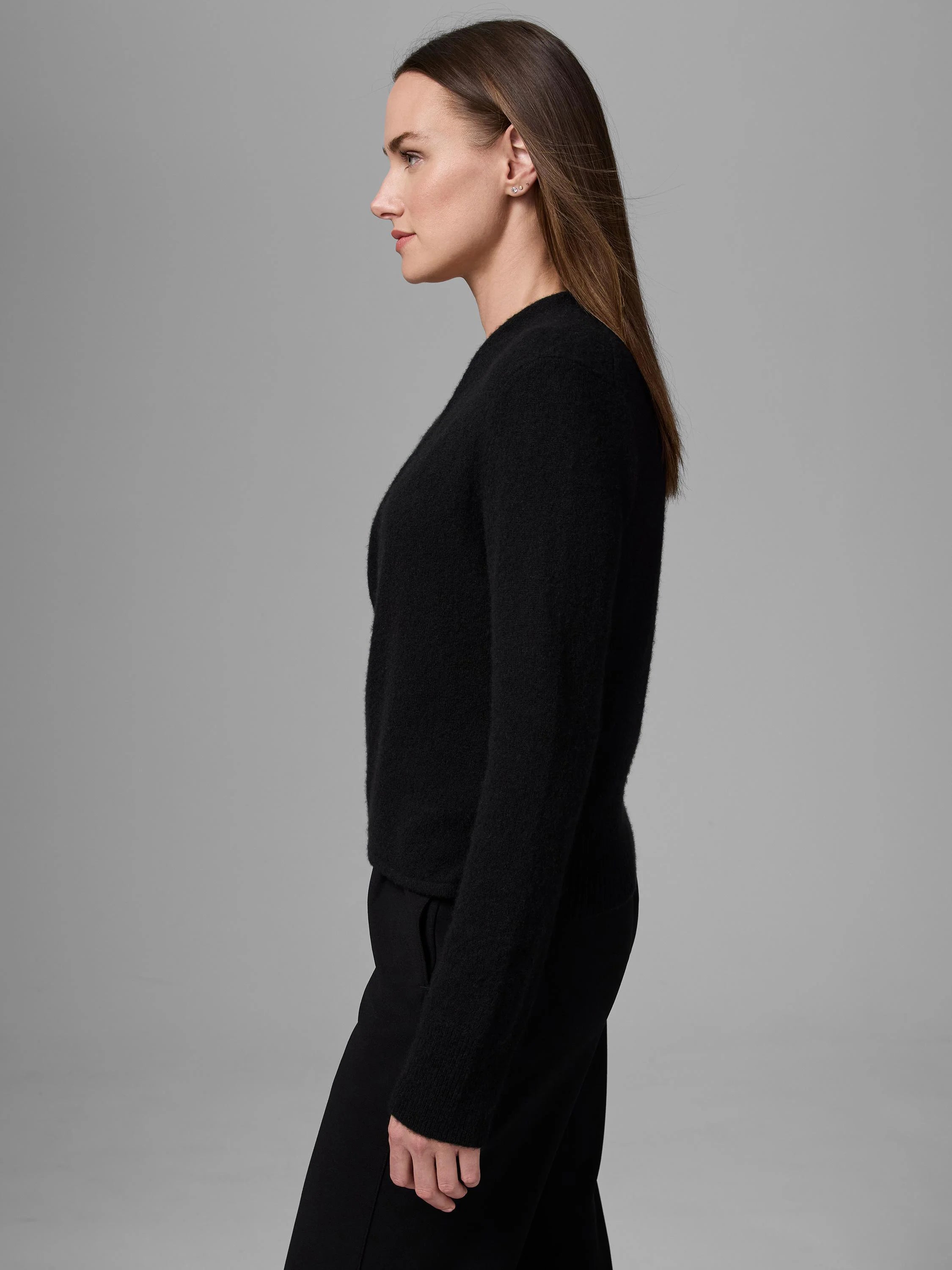 Black cashmere cardigan with a soft, fuzzy texture and long sleeves. Worn closed by a woman in profile.