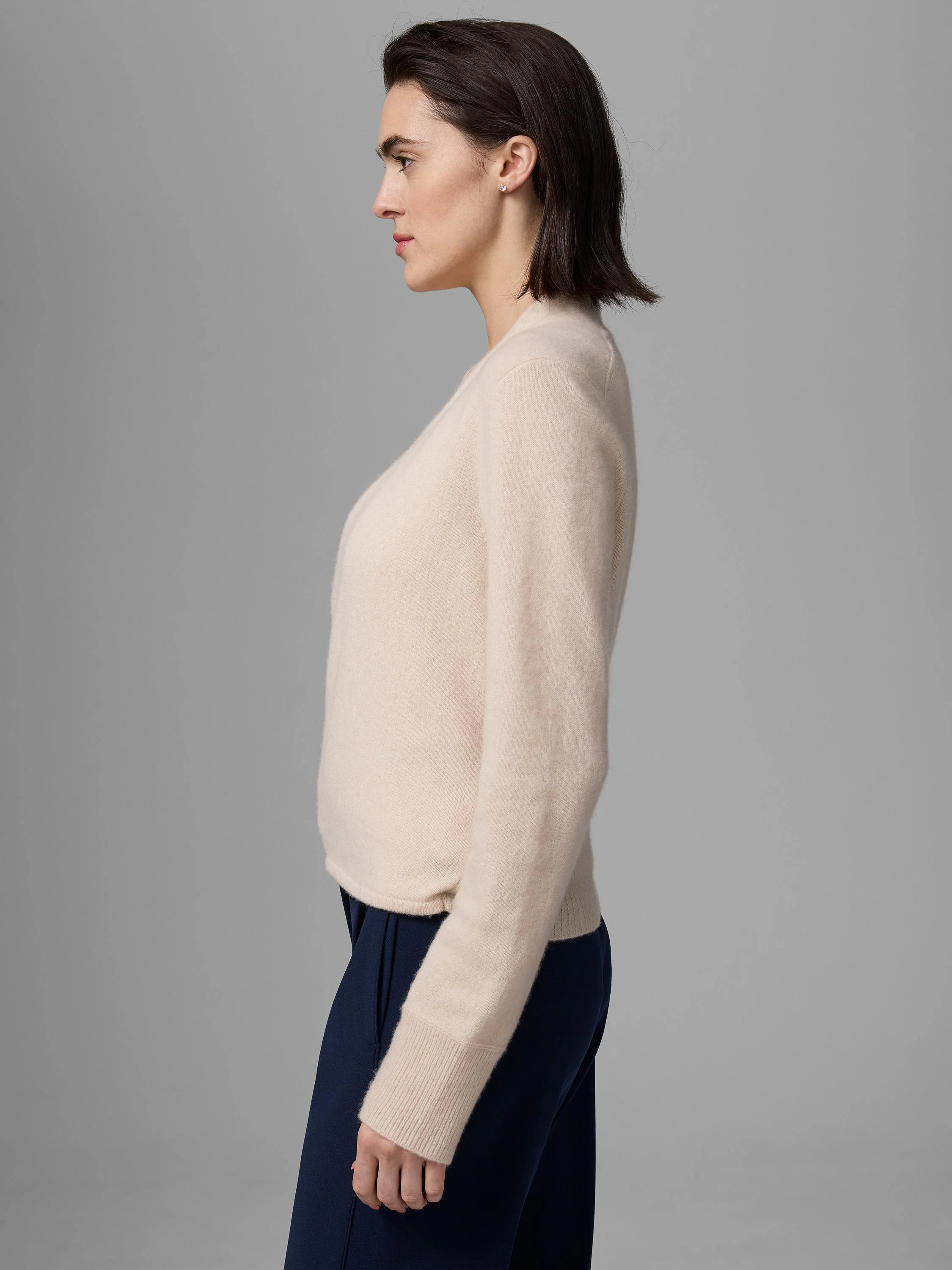 Cream cashmere cardigan with long sleeves and ribbed cuffs, worn by a woman in profile.