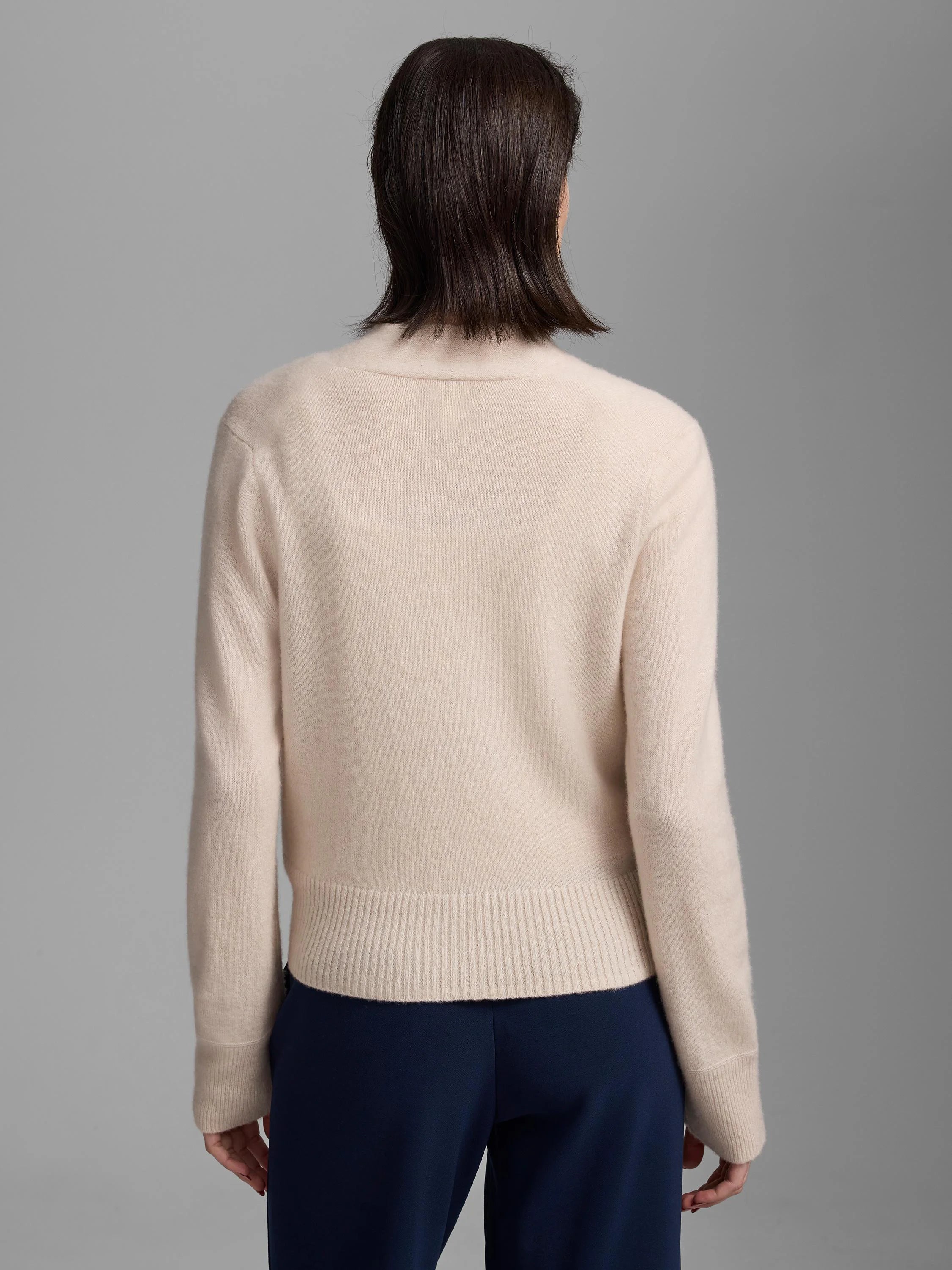 Light beige cashmere cardigan, back view. Features ribbed bottom hem and sleeve cuffs, and a rounded back neckline.