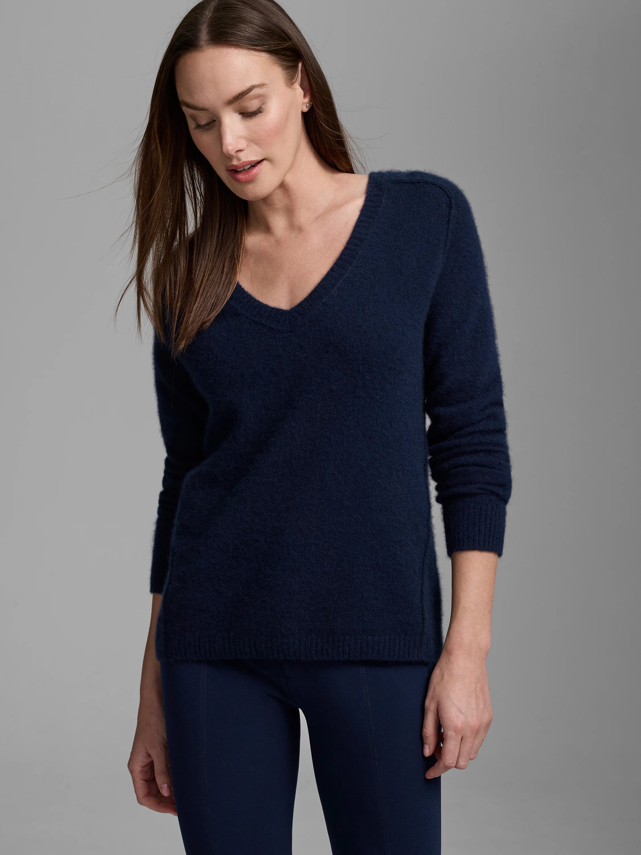 Navy blue V-neck cashmere sweater with a fuzzy texture, long sleeves, ribbed cuffs, and subtle side slits.