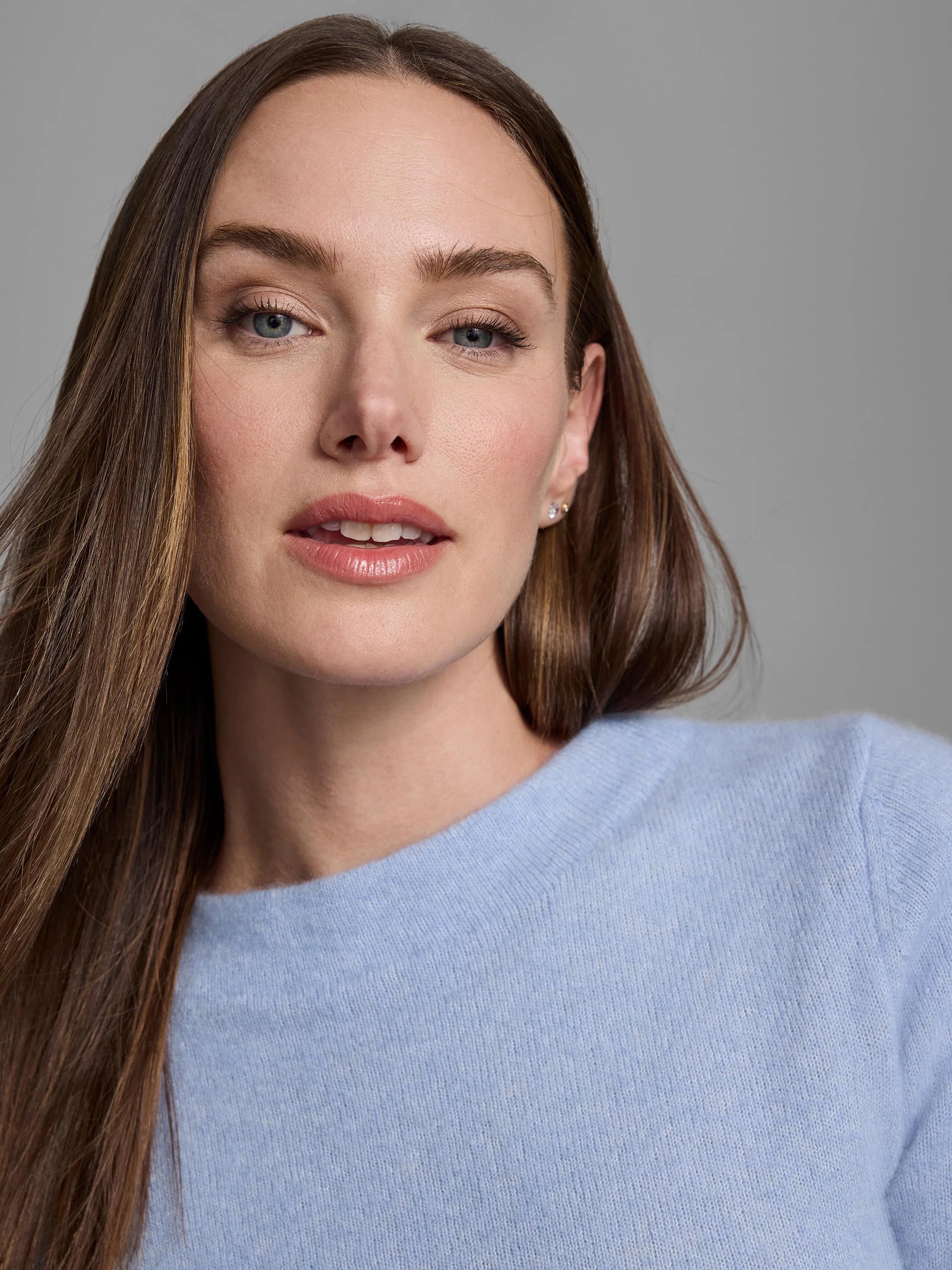 Model wears a light blue cashmere mock neck sweater, showing soft knit texture on the upper chest.