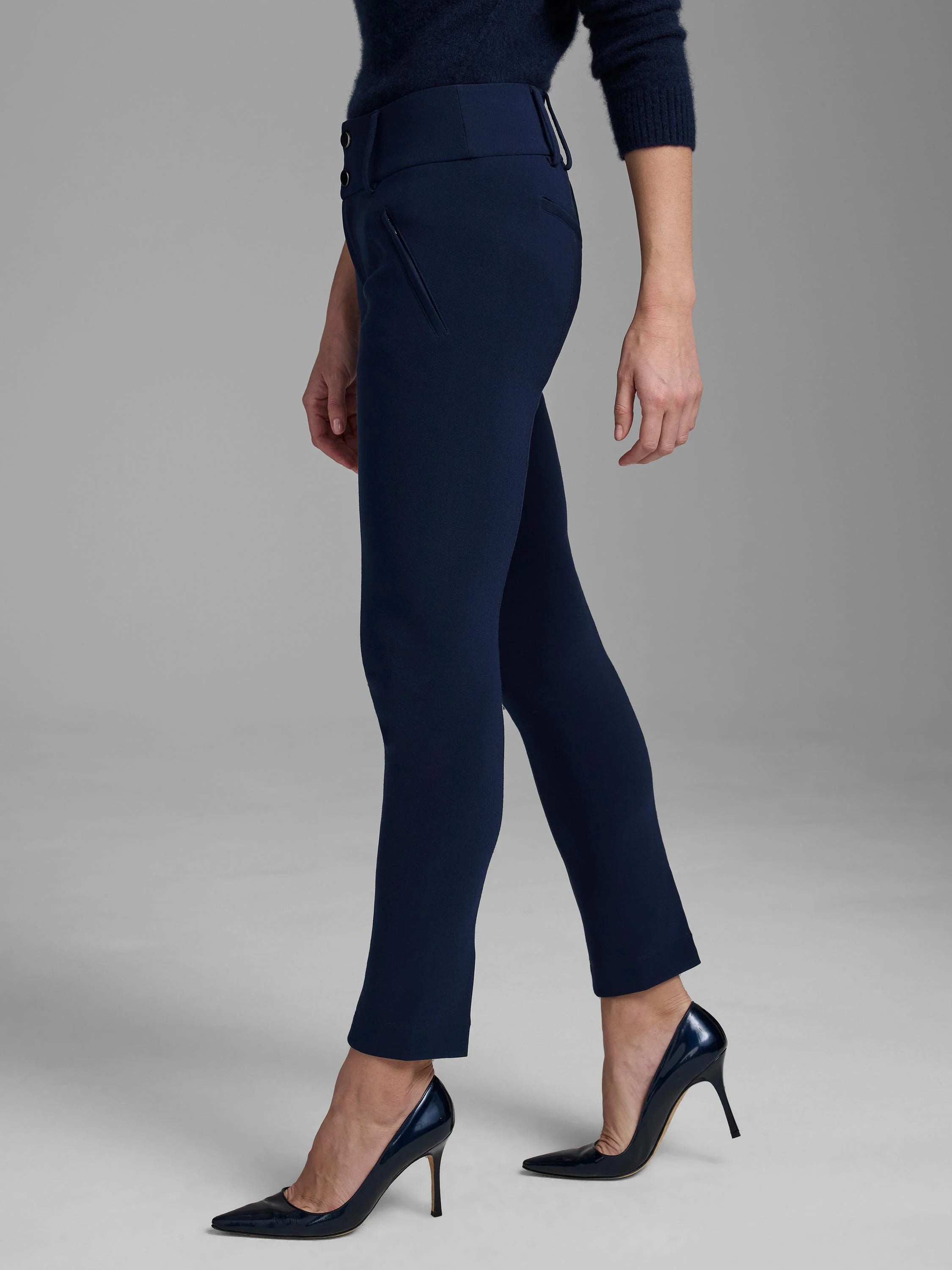 Navy slim-fit scuba knit pants with high waist, two side buttons, and angled zipper pockets. Cropped above ankles.